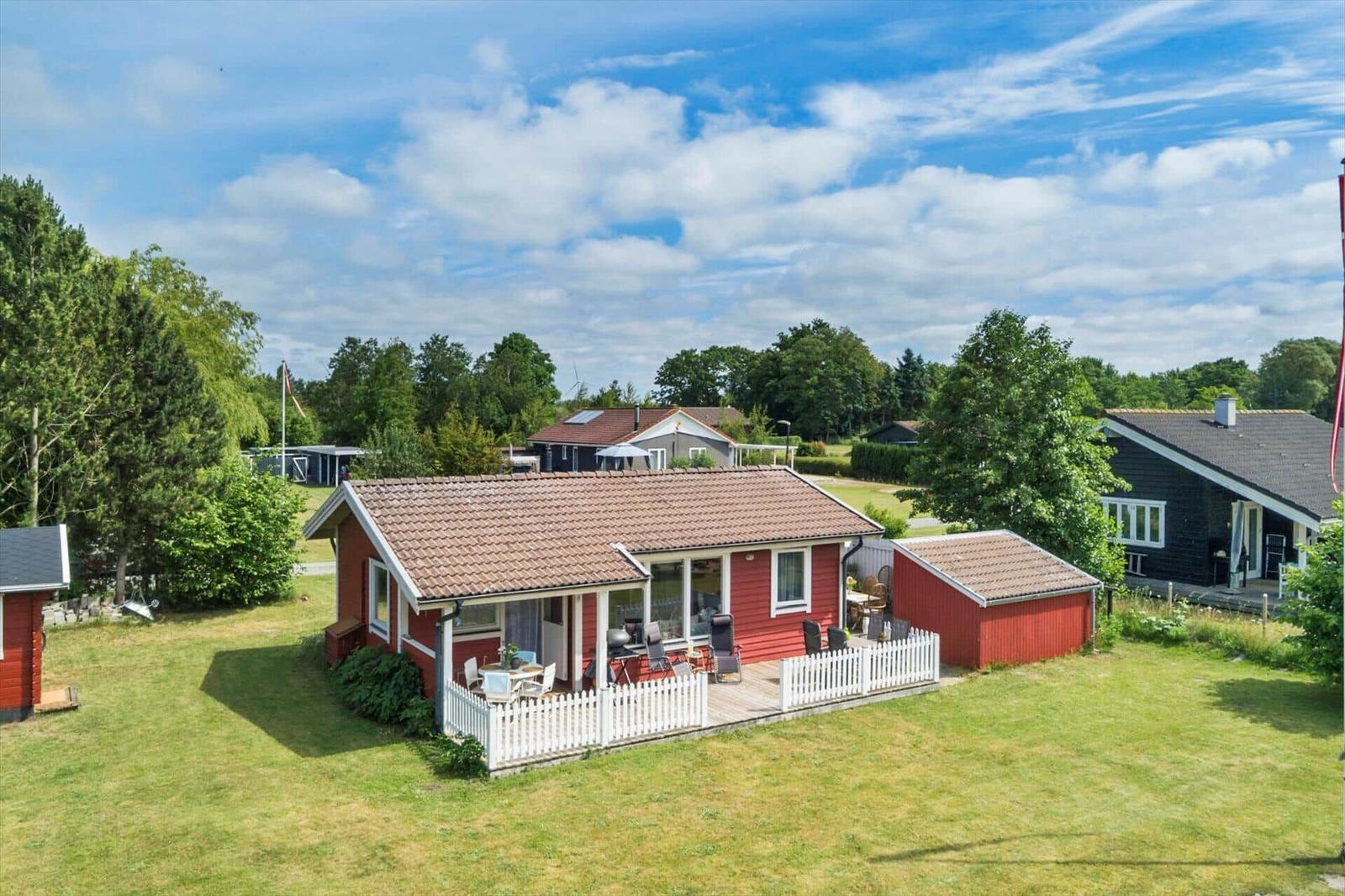 Rotes Ferienhaus mit Terrasse und Garten unter blauem Himmel.
