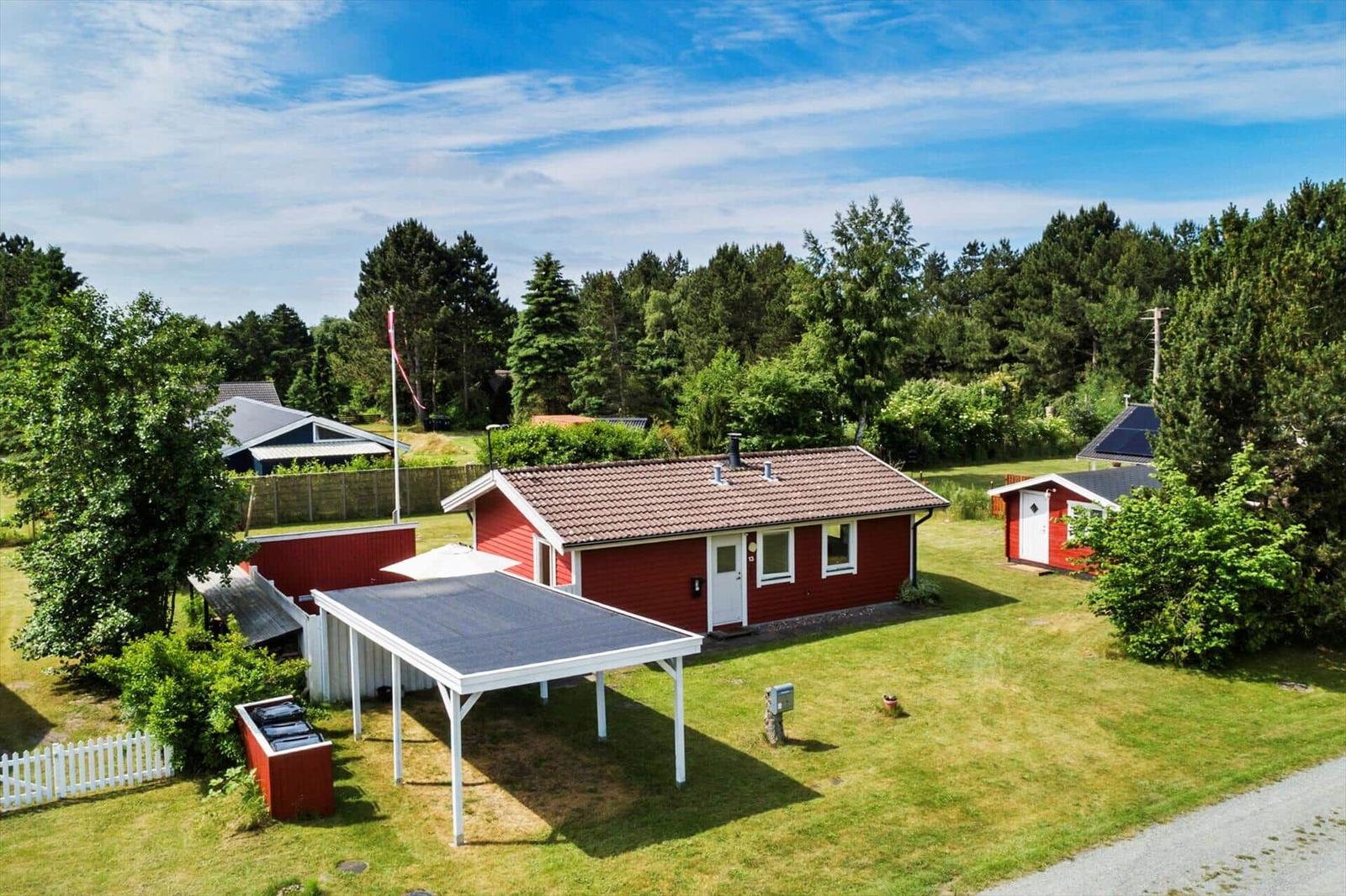 Rotes Haus mit Garage und Garten. Umgeben von Bäumen und Grasfläche.