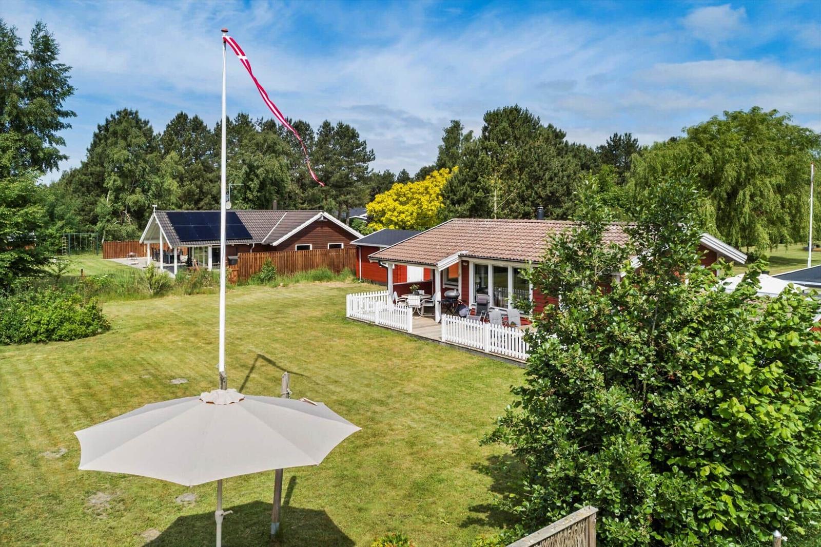 Roter Holzhaus mit weißem Zaun und Garten unter blauem Himmel.
