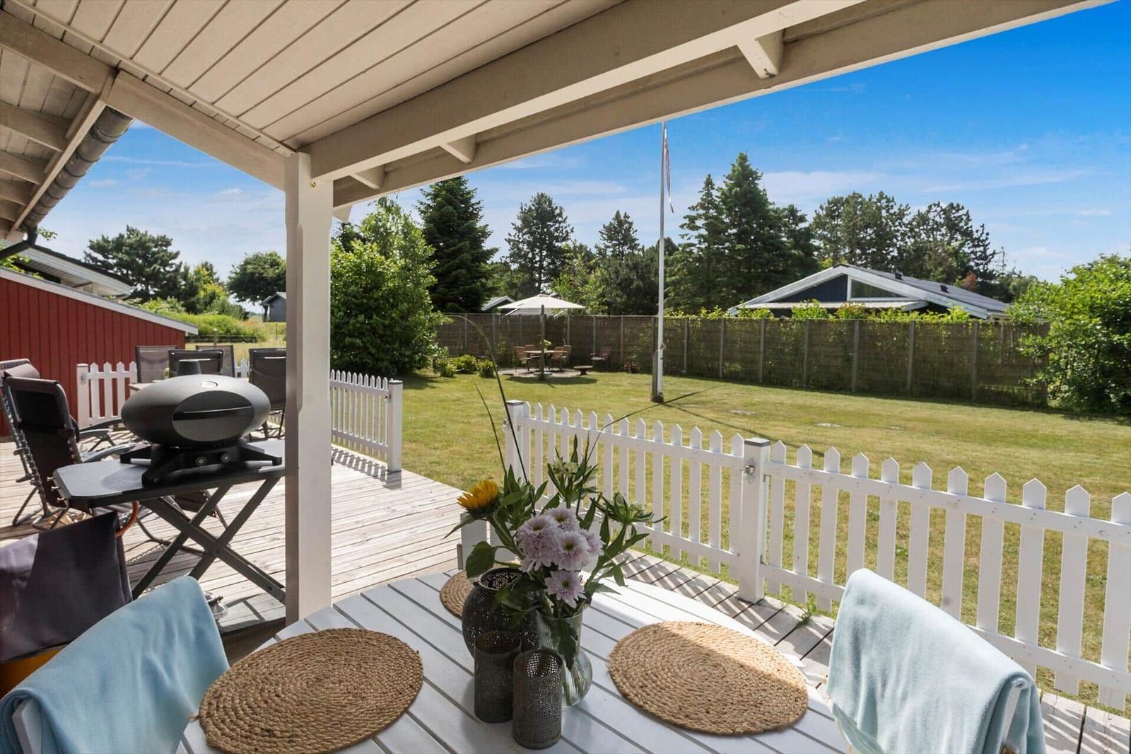 Terrasse mit Tisch, Stühlen und Grill. Hinterhof mit weißen Zaun und Grünfläche.
