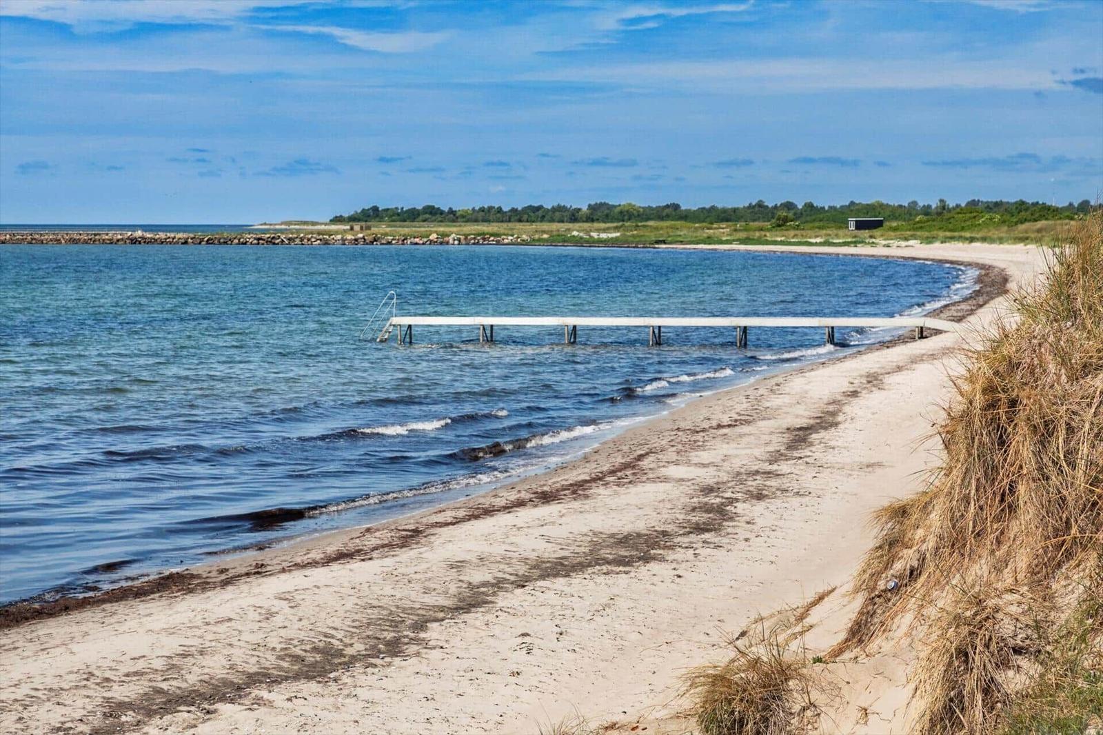 Strand mit weißem Steg ins Wasser, Sandufer und Grasbewuchs