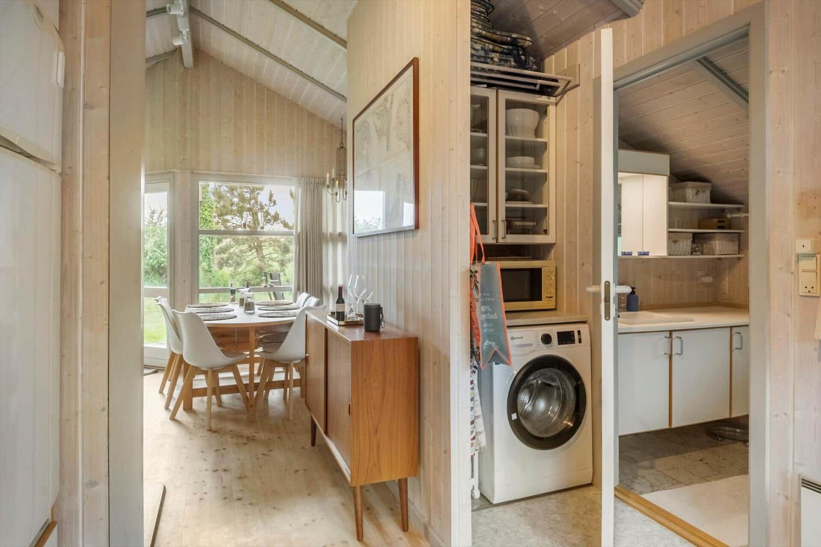 Küche mit Waschmaschine, Essbereich mit Tisch und Stühlen, Holzwände und Fenster zum Garten.