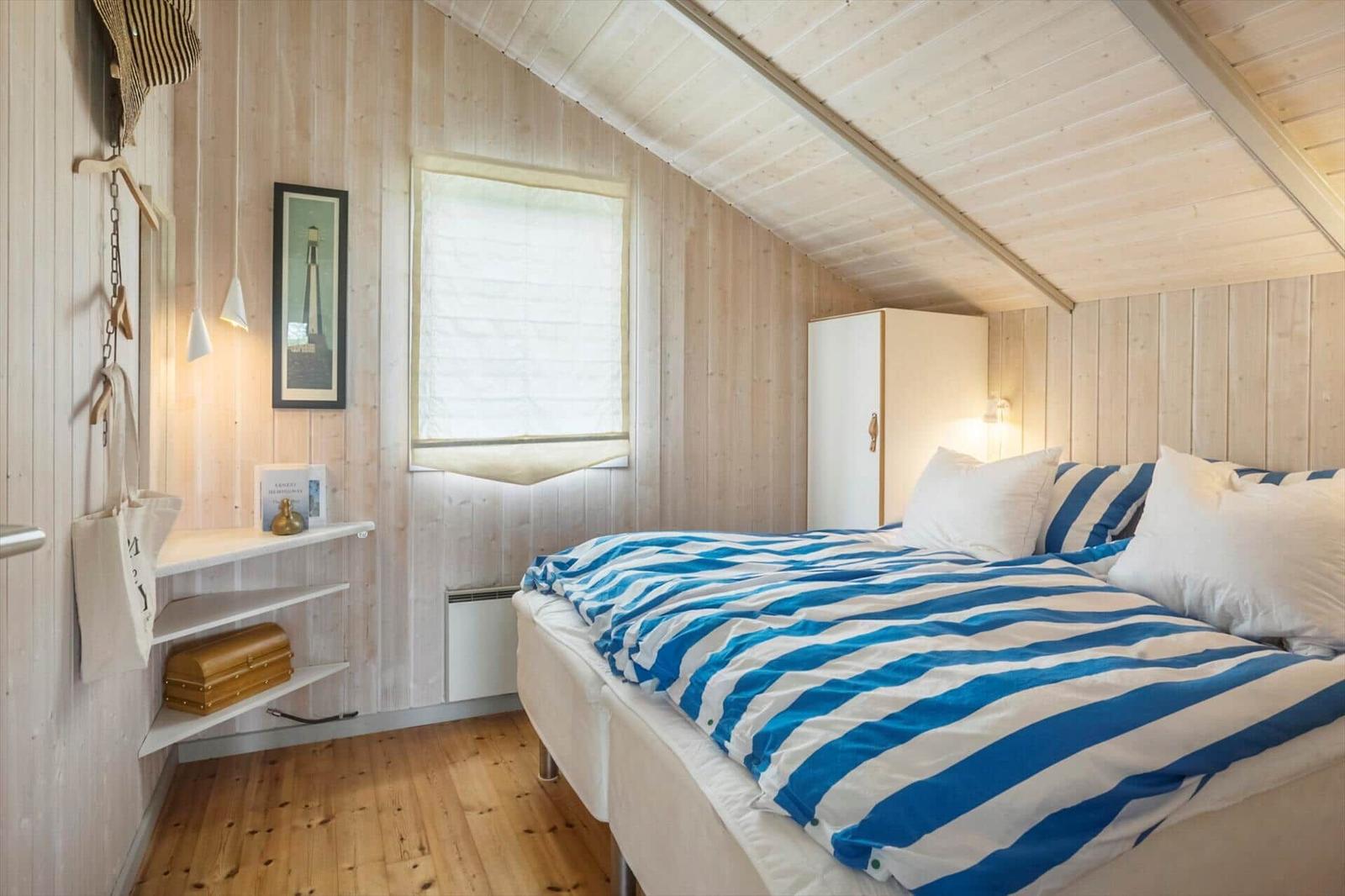 Schlafzimmer mit Holzwand, Bett mit blau-weißem Bettzeug und kleinem Schrank.