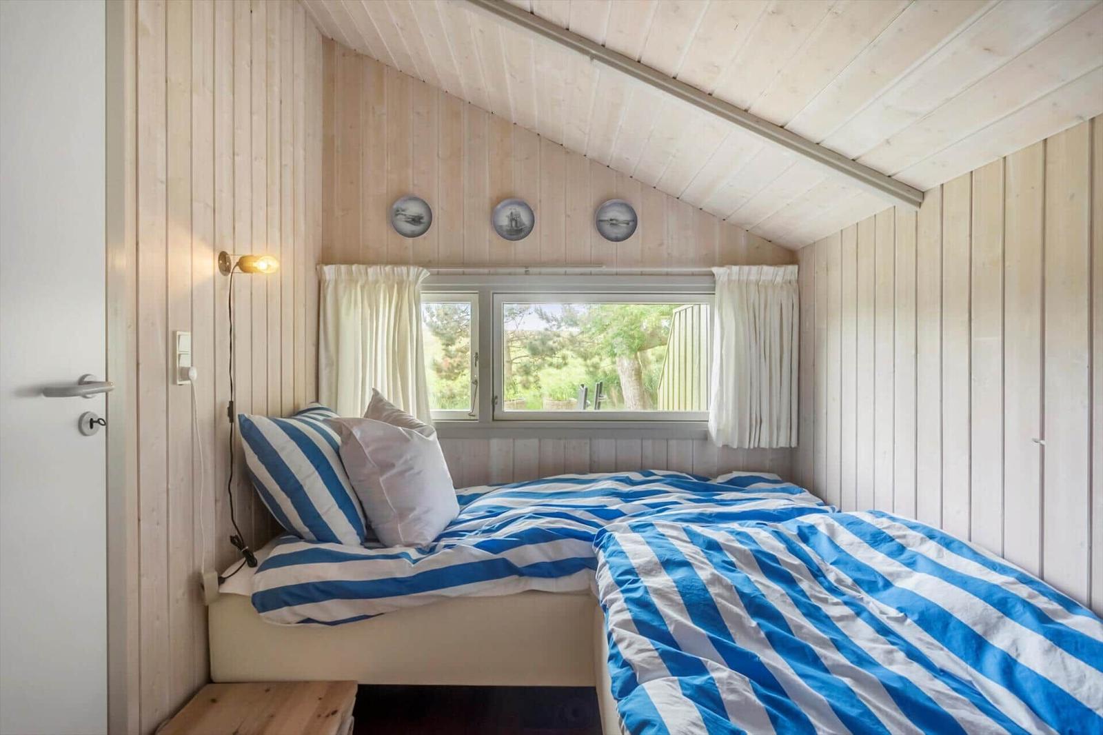 Schlafzimmer mit zwei Betten, Holzwand und Fenster mit Blick auf Grün.