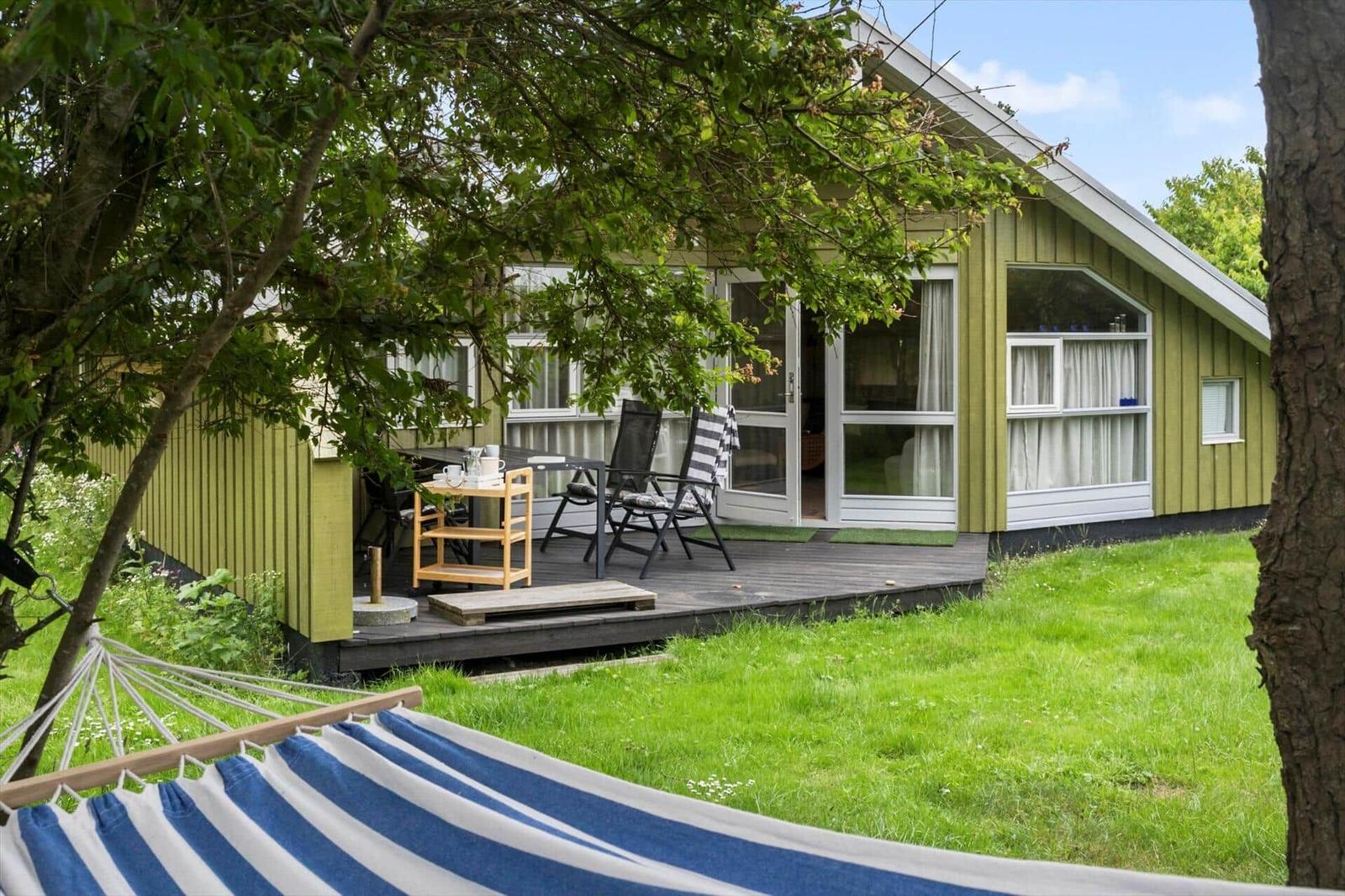 Grünes Ferienhaus mit Terrasse, Garten und Hängematten im Vordergrund.