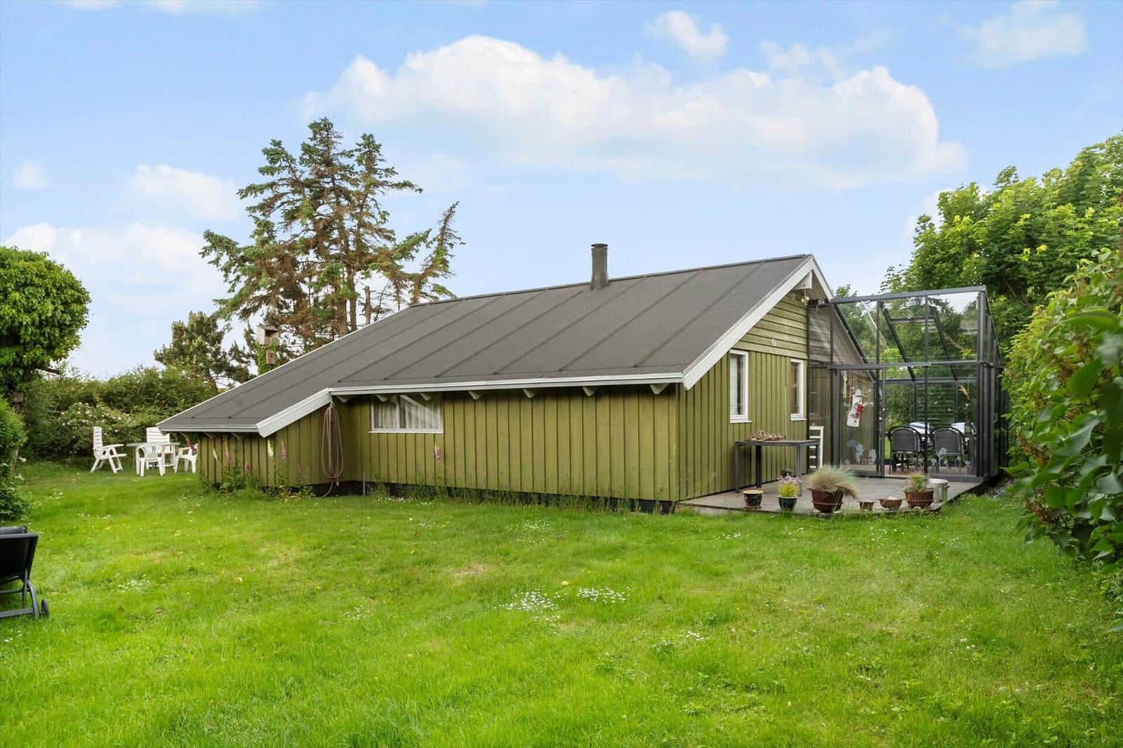 Grünes Holzhaus mit Terrasse und Garten. Glasveranda und weiße Gartenmöbel.