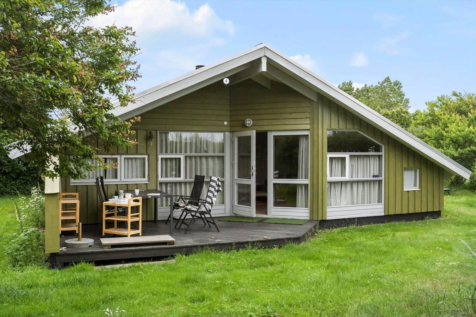 Grünes Holzhaus mit Terrasse, Garten und Fenstern mit Vorhängen.