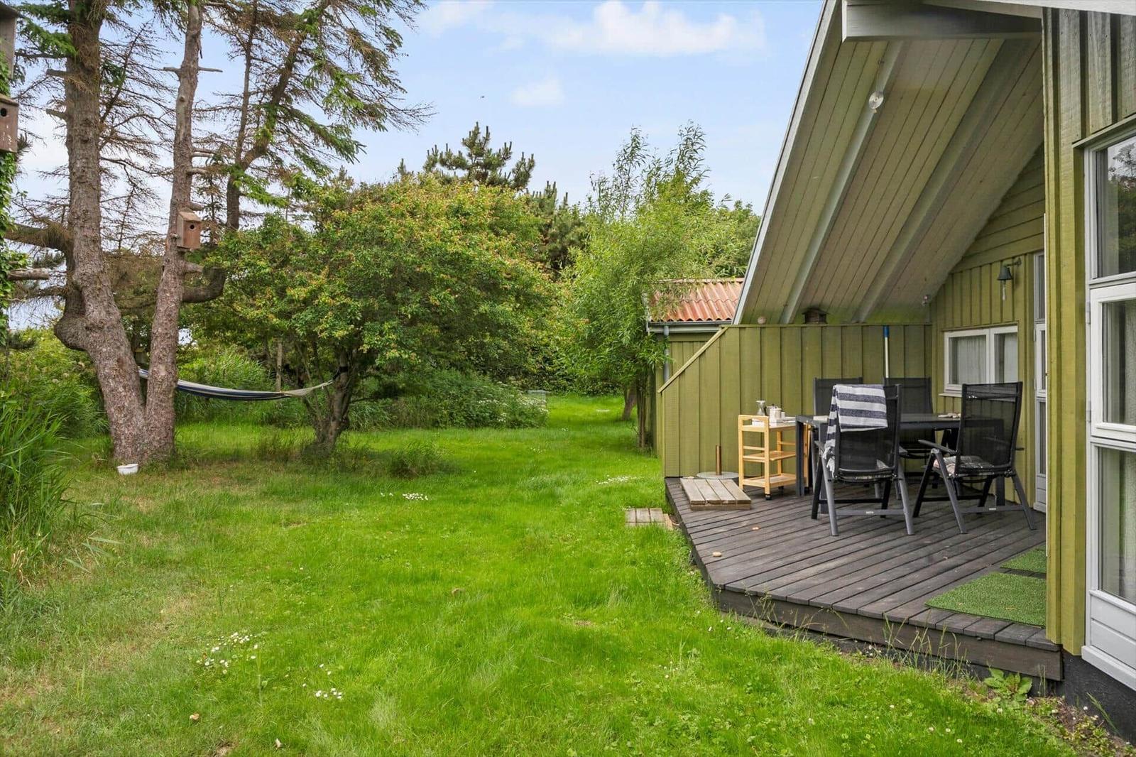Grüner Garten mit Hängemöbel und Holzterrasse mit Sitzgruppe neben Haus.