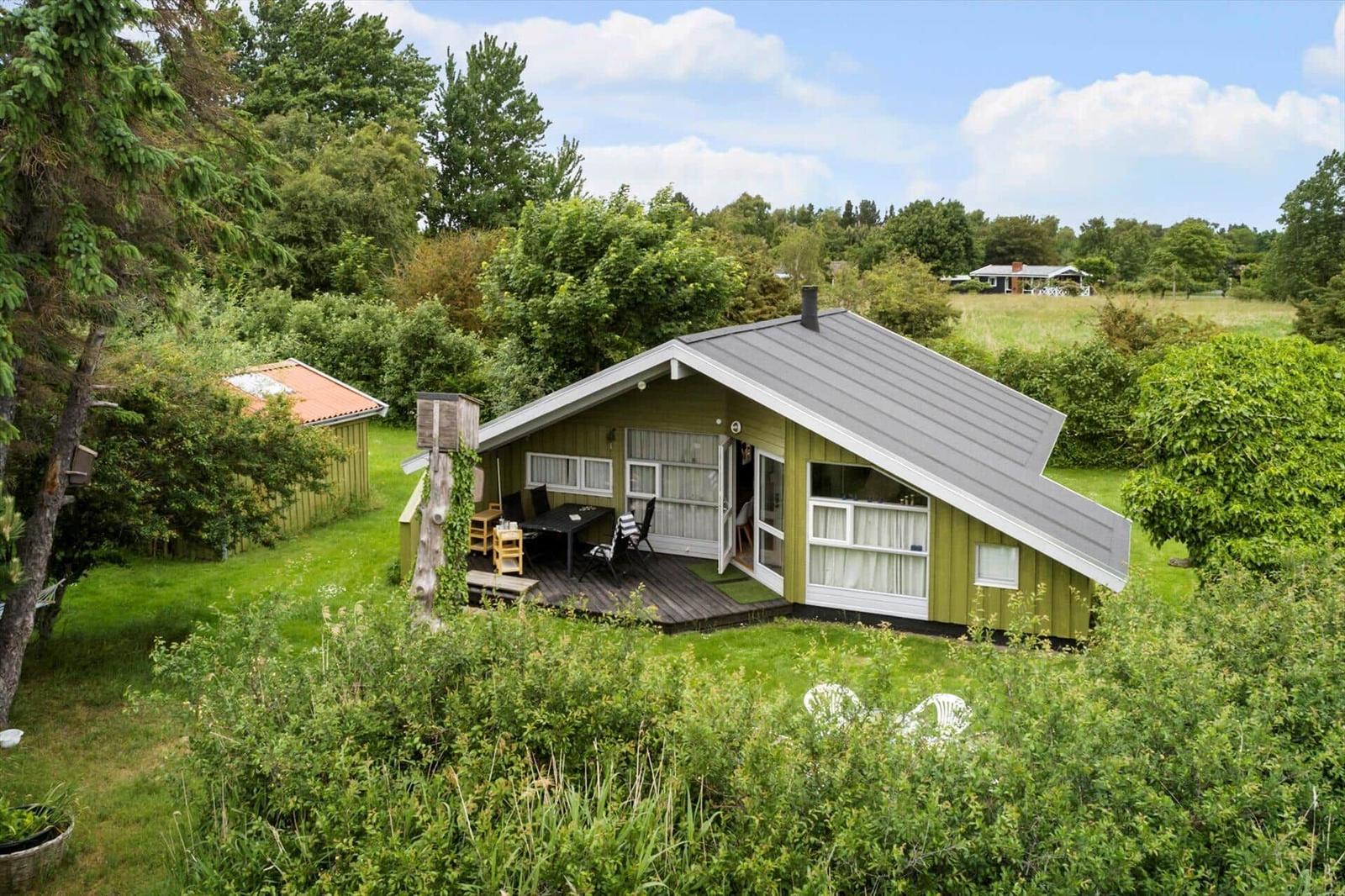 Ein grünes Ferienhaus mit Terrasse und Garten. Umgeben von Bäumen und Gras.