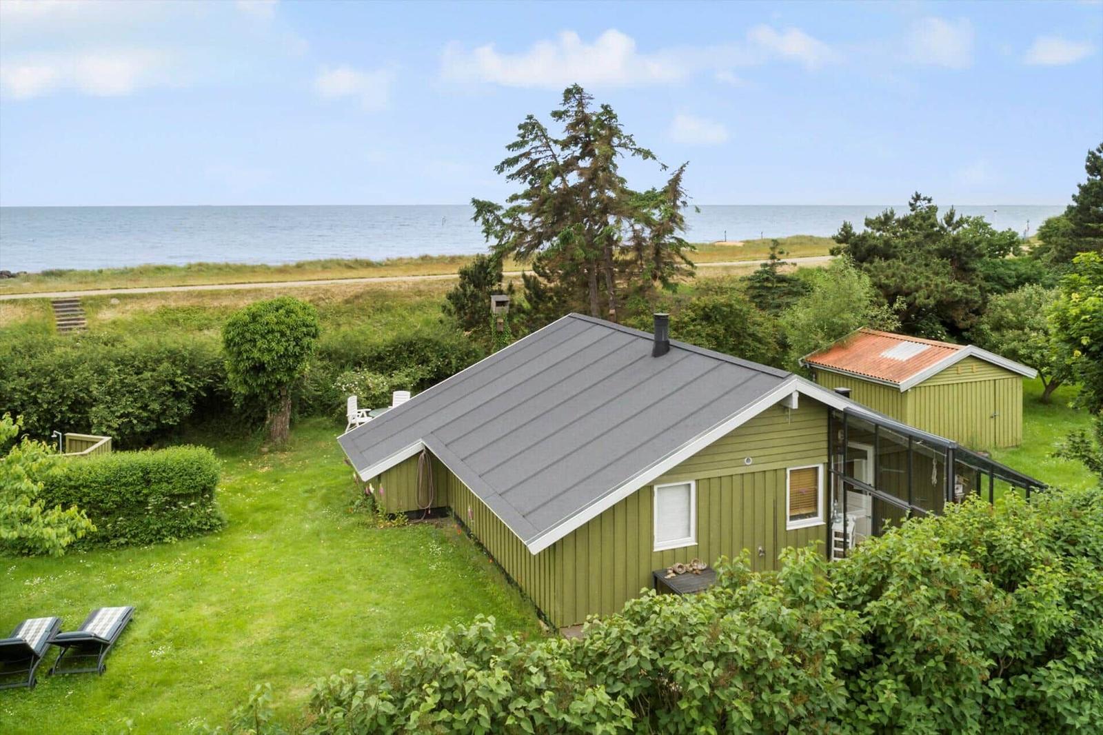 Grünes Ferienhaus mit Garten und Meerblick. Terrasse und Liegestühle im Freien.