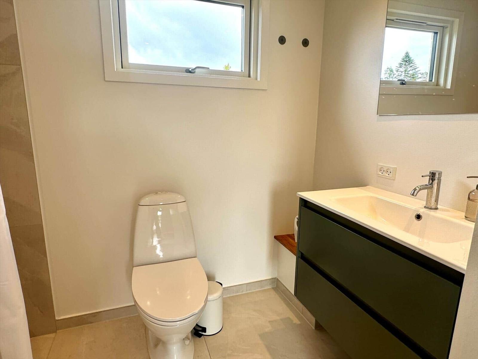 Badezimmer mit Toilette, Waschbecken und Fenster. Spiegel und Holzbank sind vorhanden.