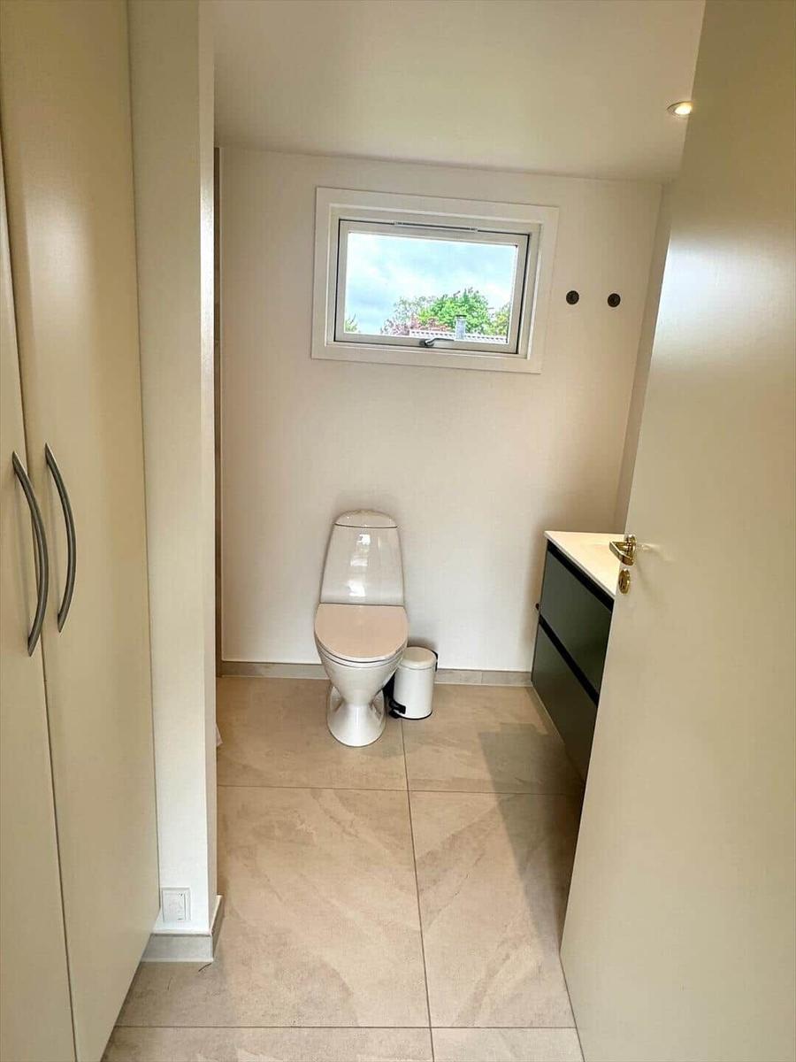 Toilettenraum mit Fenster, WC, Mülleimer und Waschtisch.