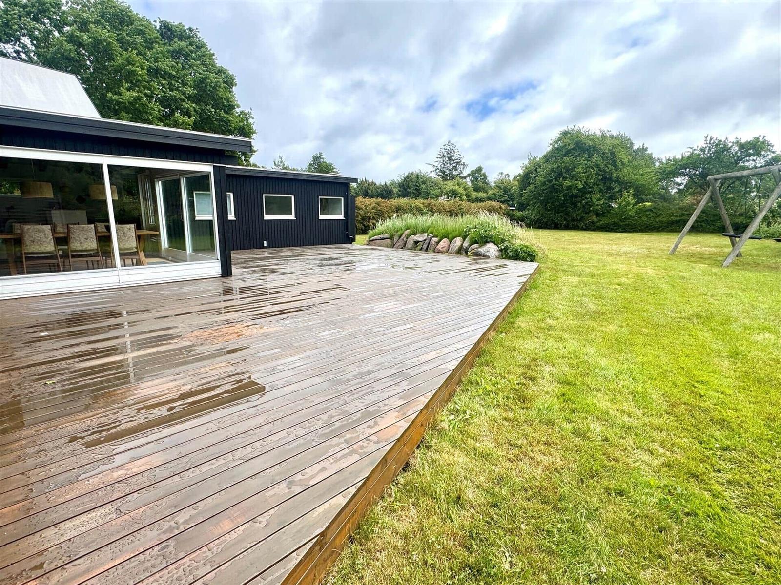 Holzterrasse neben modernem Haus mit Garten und Schaukel.