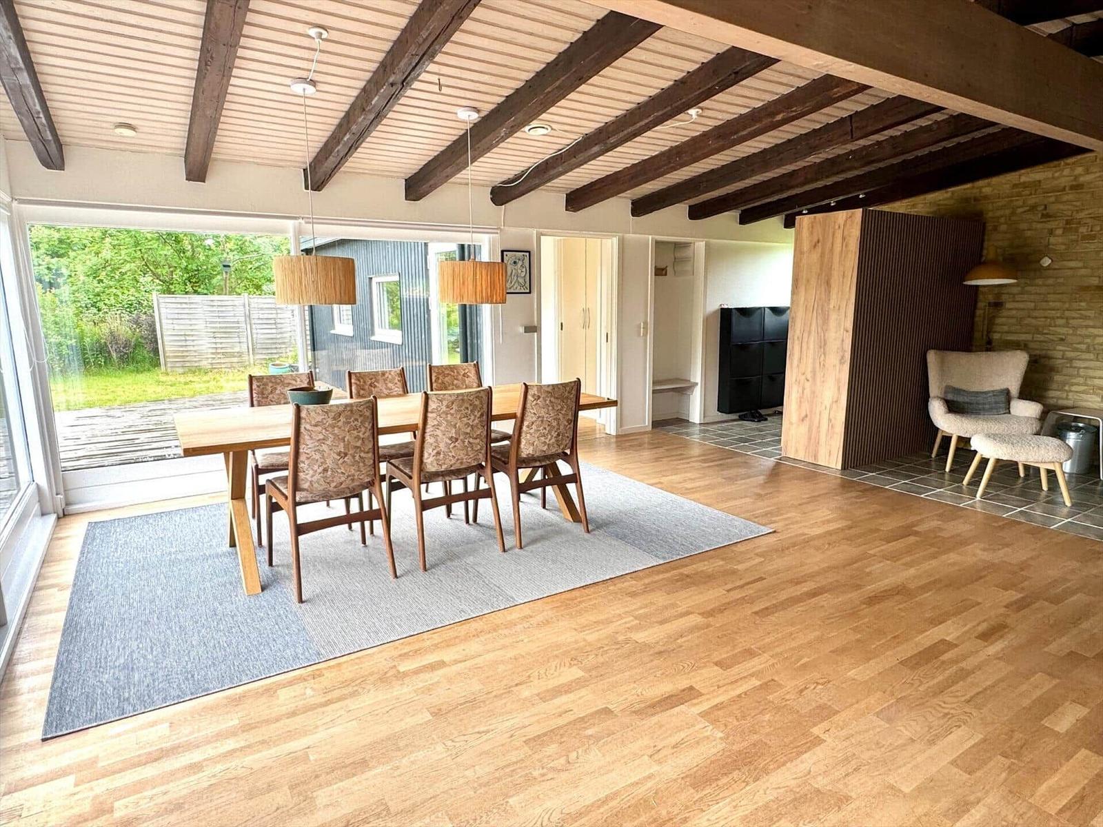Essbereich mit Tisch, Stühlen und Blick auf Garten. Holzboden und Deckenbalken.