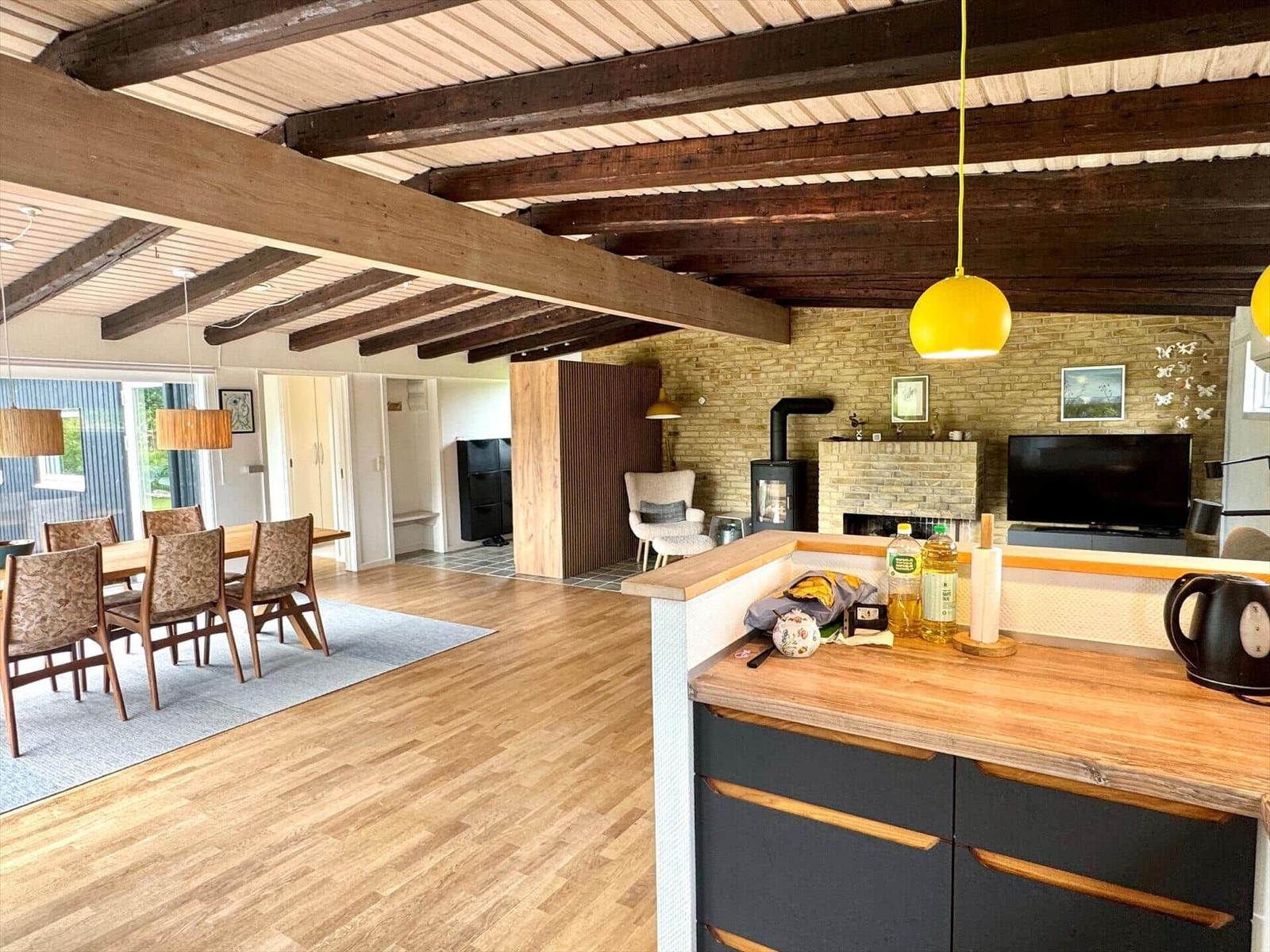 Großes Wohn- und Esszimmer mit Holzbalken, Kamin und Kücheninsel.