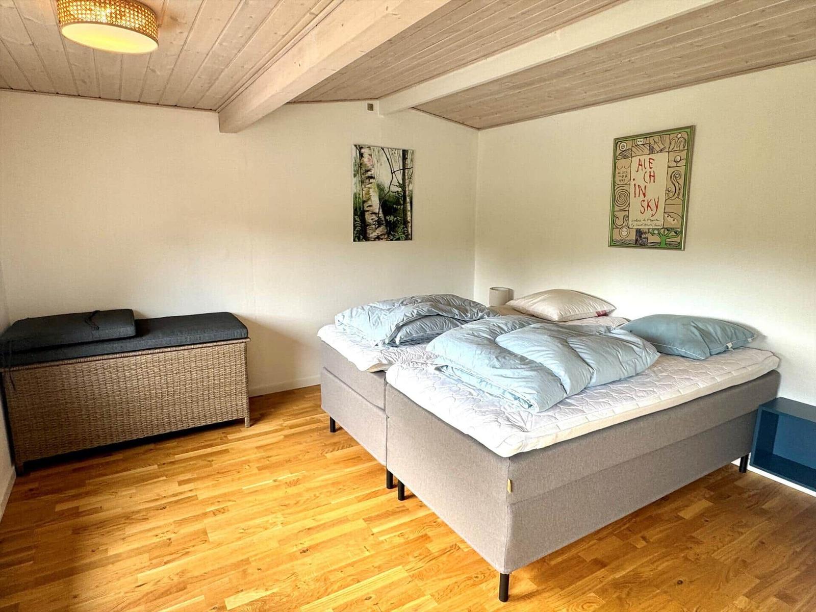 Schlafzimmer mit Bett, Holzboden und Deckenbalken. Wandbild und Kissen sind sichtbar.