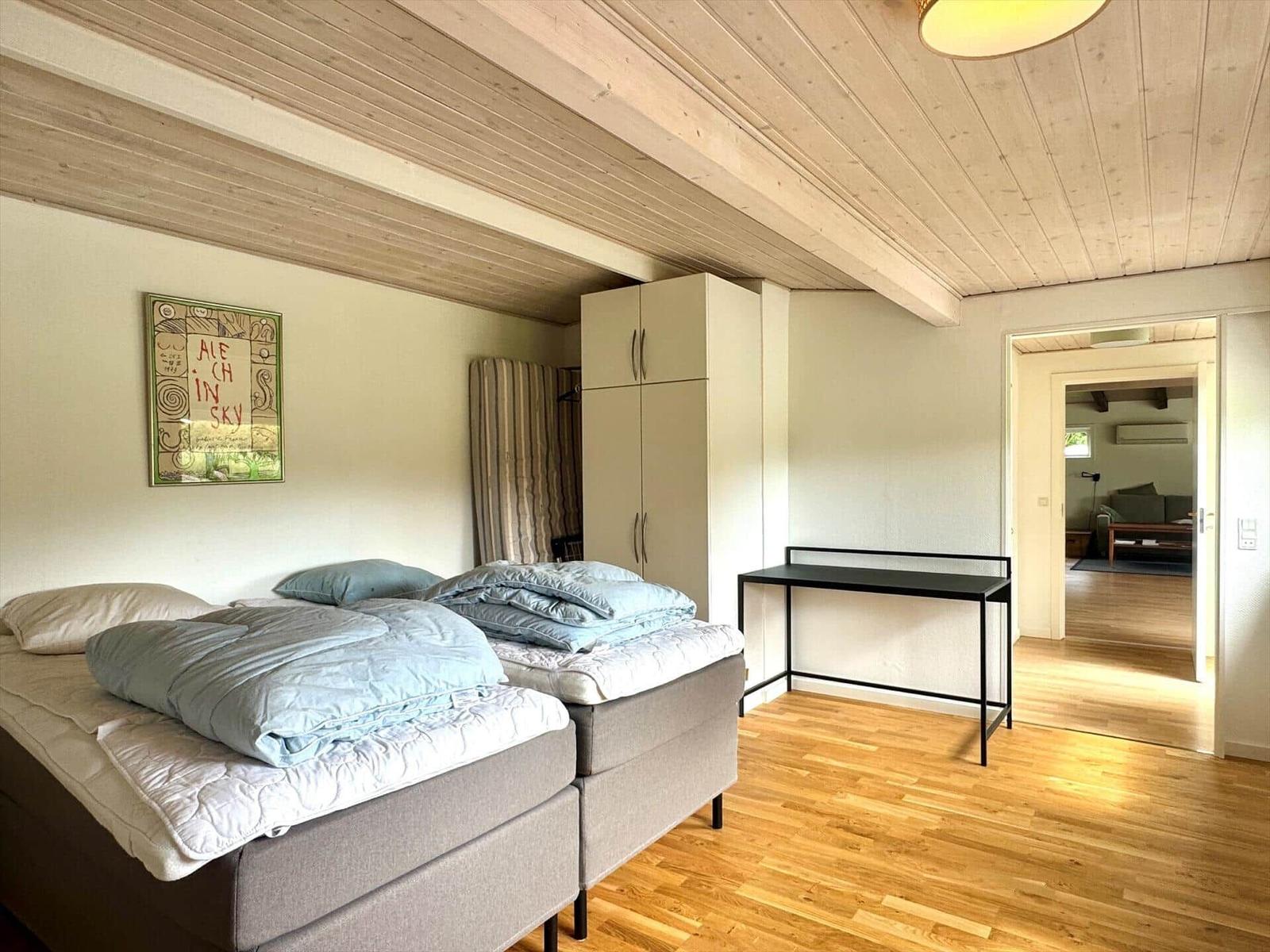 Zwei Betten, Schrank und Tisch in einem Raum mit Holzboden und Decke.