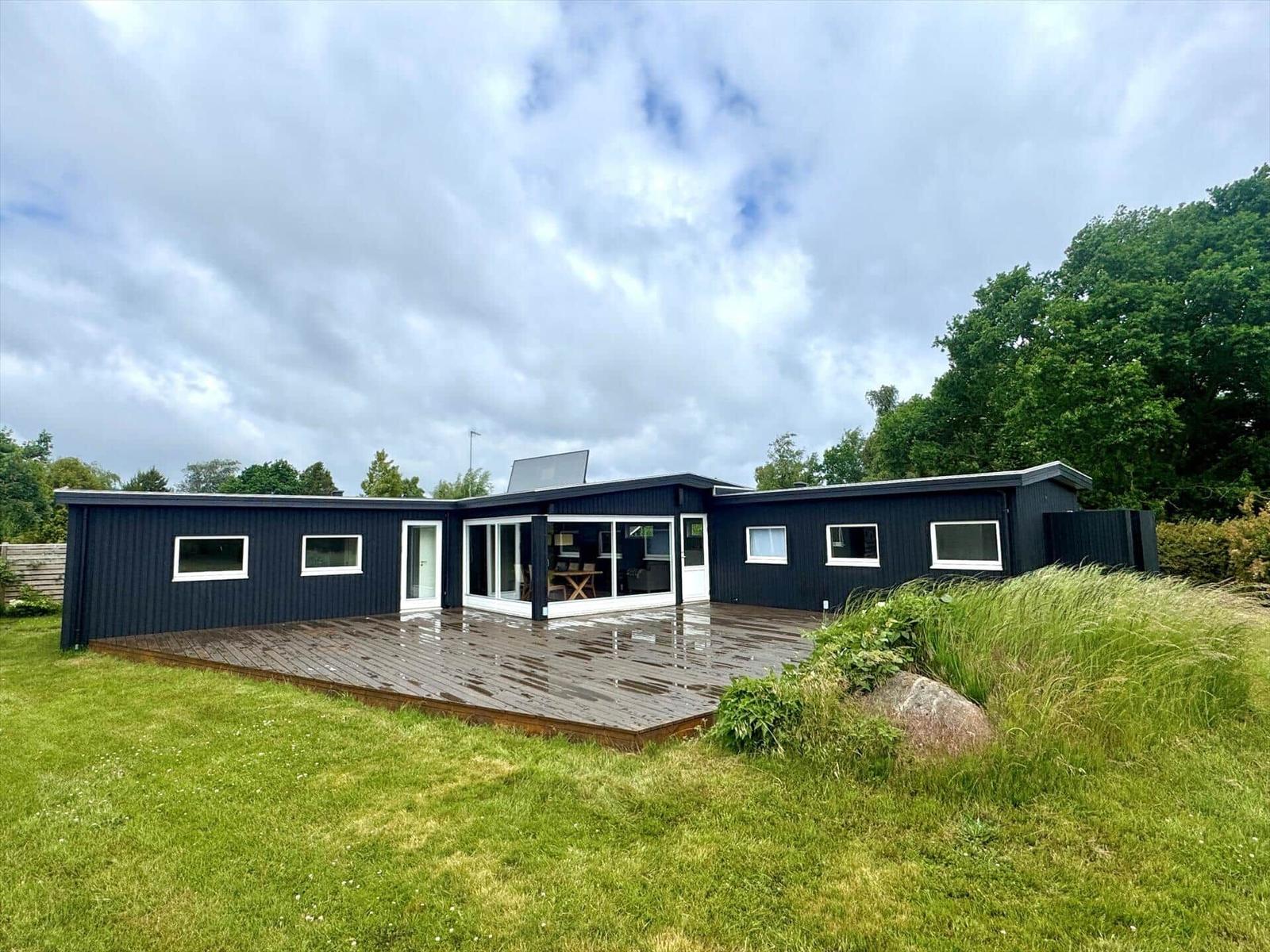 Moderne schwarze Villa mit Holzterrasse und Garten. Große Fensterfront.