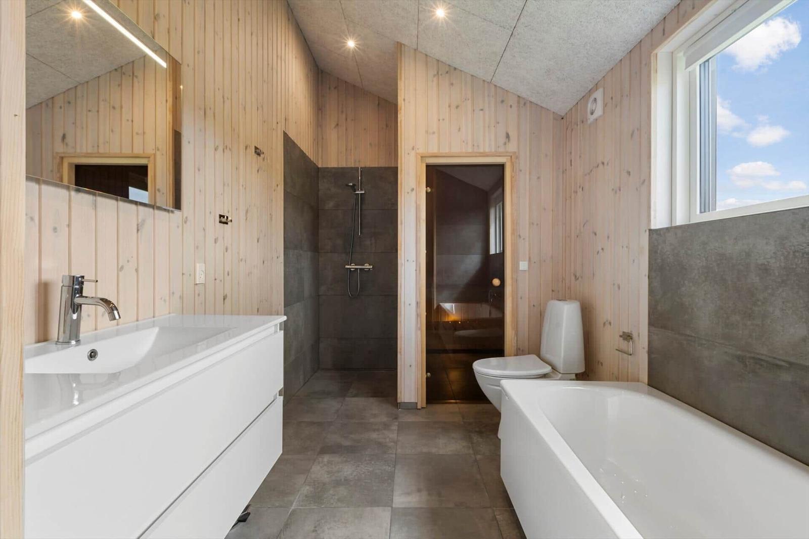 Bathroom with bathtub, toilet, shower, and sink. Wooden walls and window with sky view.
