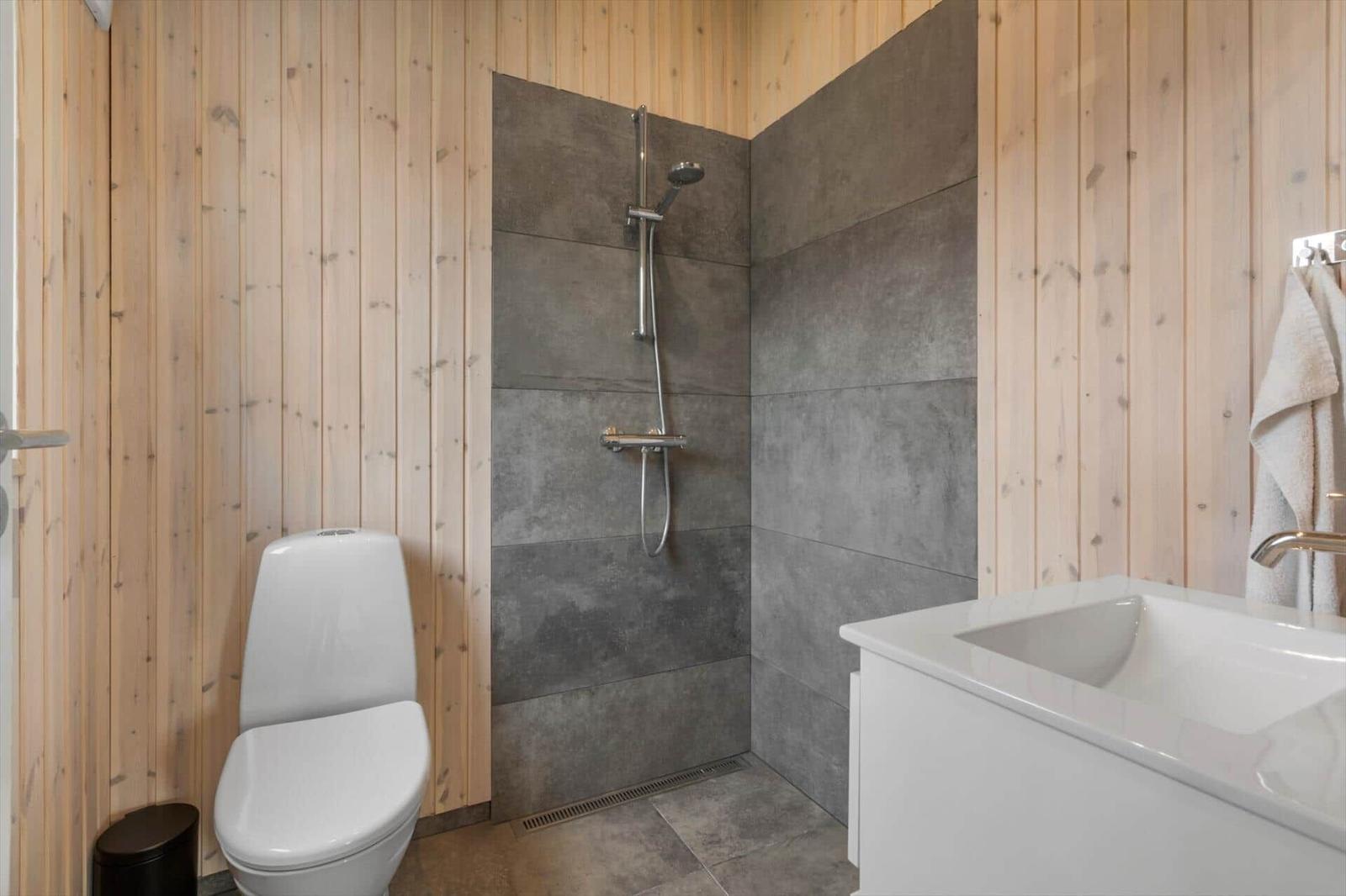 Bathroom with shower, toilet, and sink. Wooden walls and gray tiles.