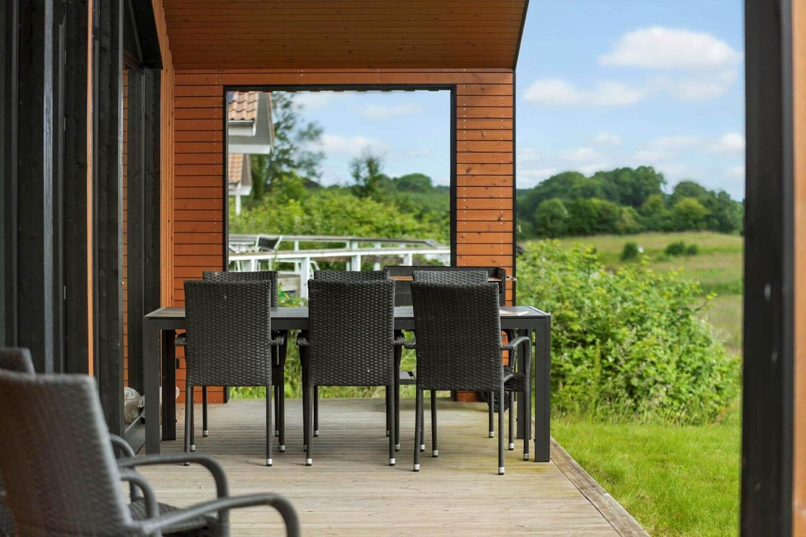 Terrace with dining table and chairs. View of green landscape and sky.