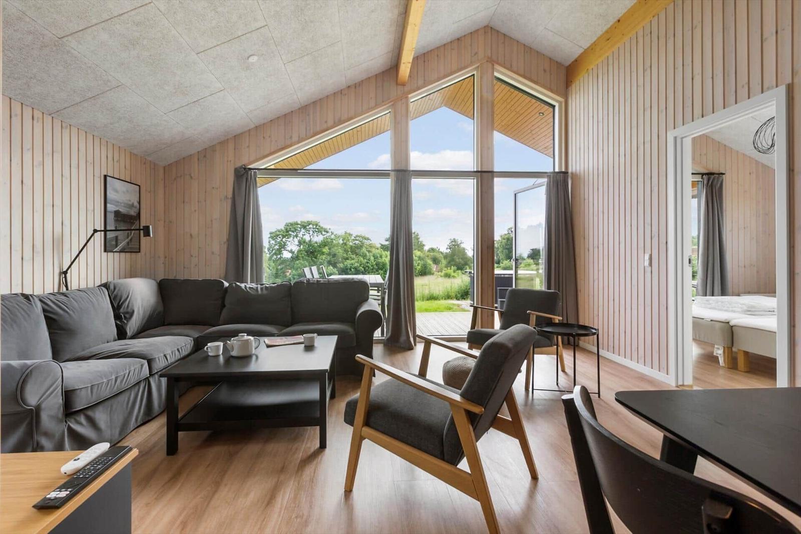 Living room with sofa, chairs, and view of garden. Bedroom visible in background.