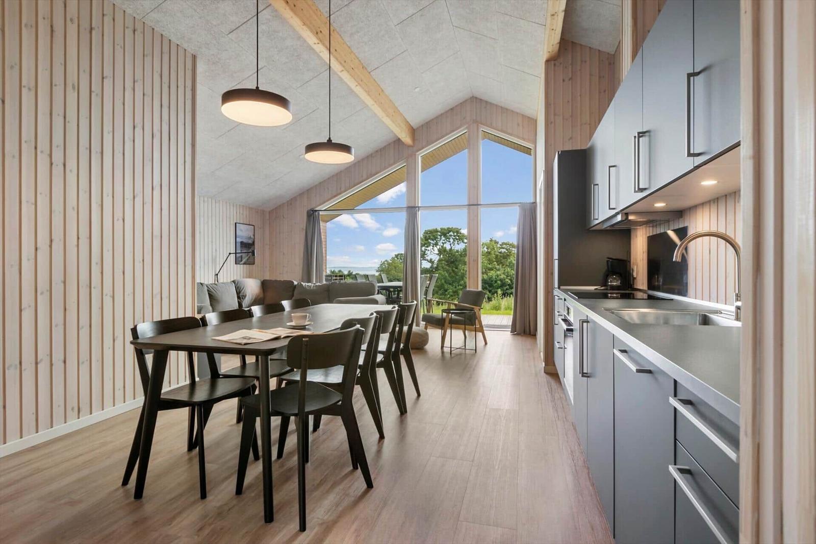 Modern kitchen and dining area with wooden wall and large window view.