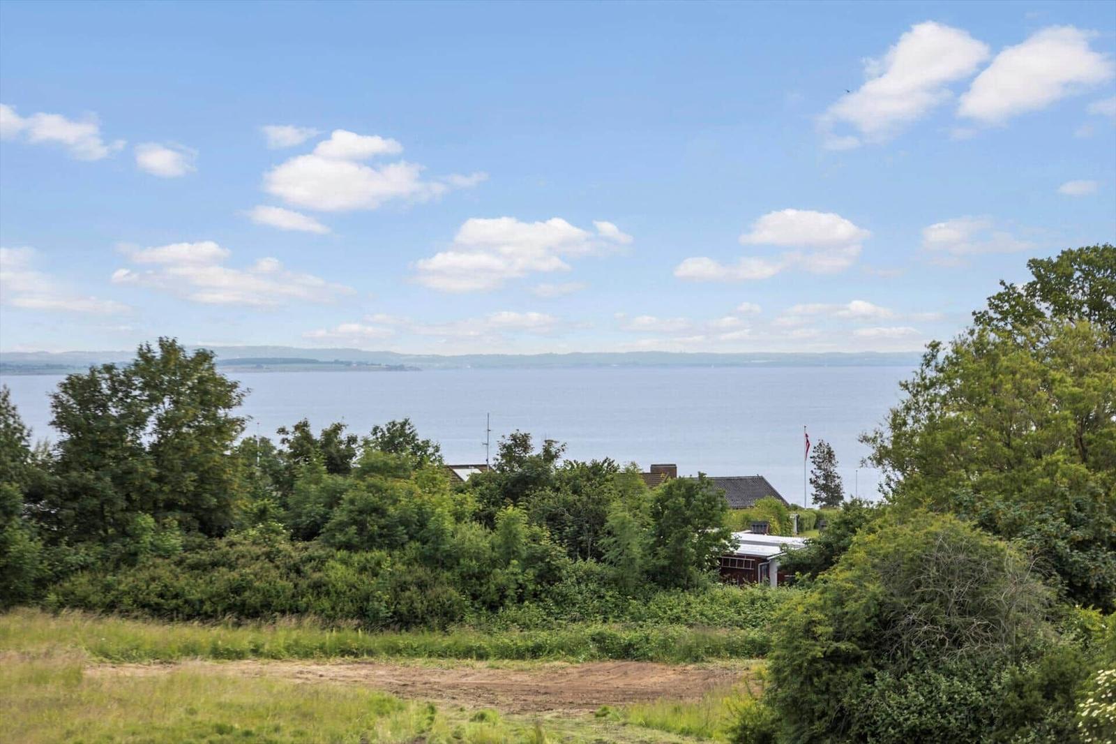 Wide view of a lake with trees and a house in the foreground.
