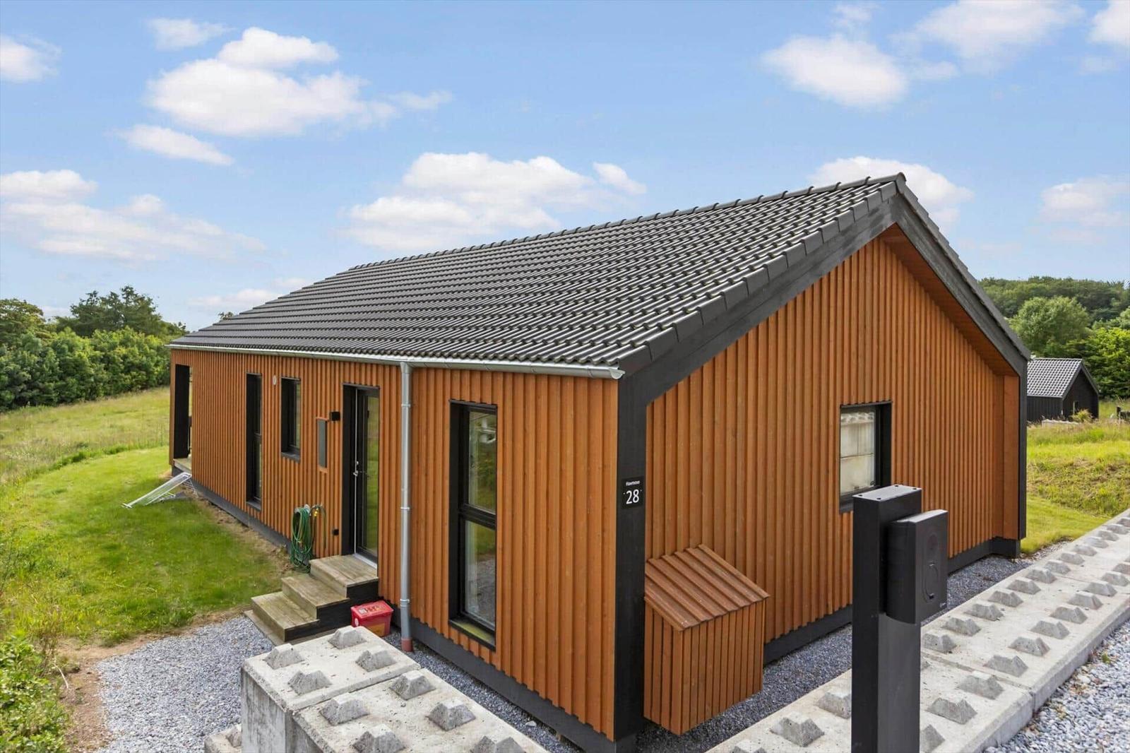 Modern wooden cabin with roof and windows. Lawn and driveway.