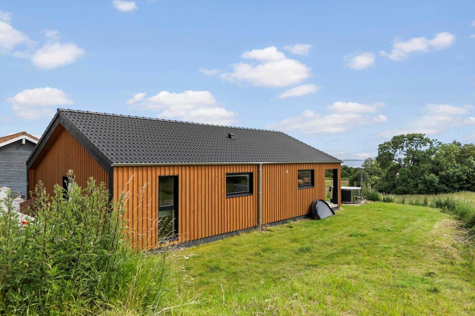 Modern wooden cabin with dark roof on green lawn under blue sky.