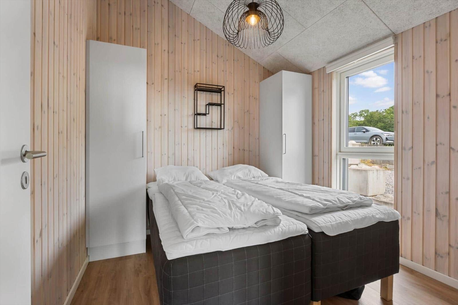 Room with two beds, wooden walls, and window view of the garden.