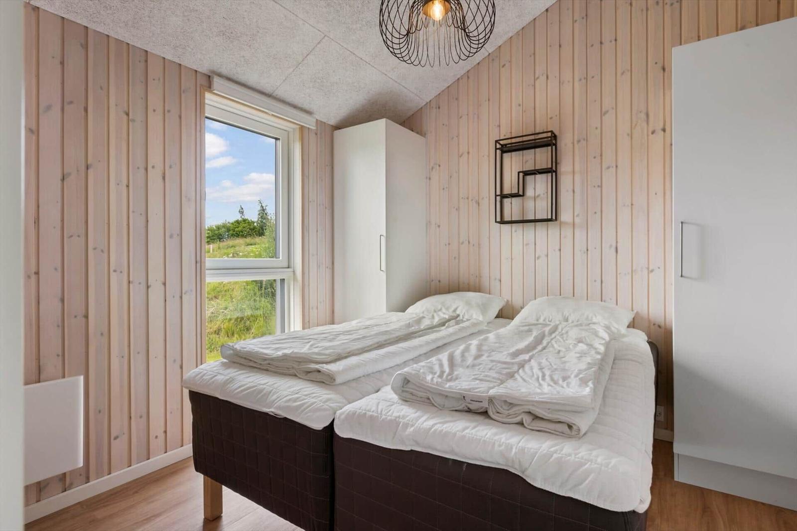Two beds with white bedding, wooden walls, and window with view of grass.