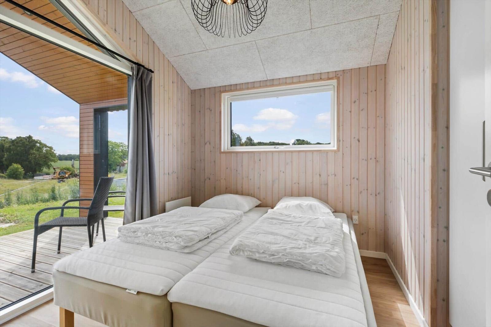 Two beds with white bedding, wooden walls, and window with view of green field.