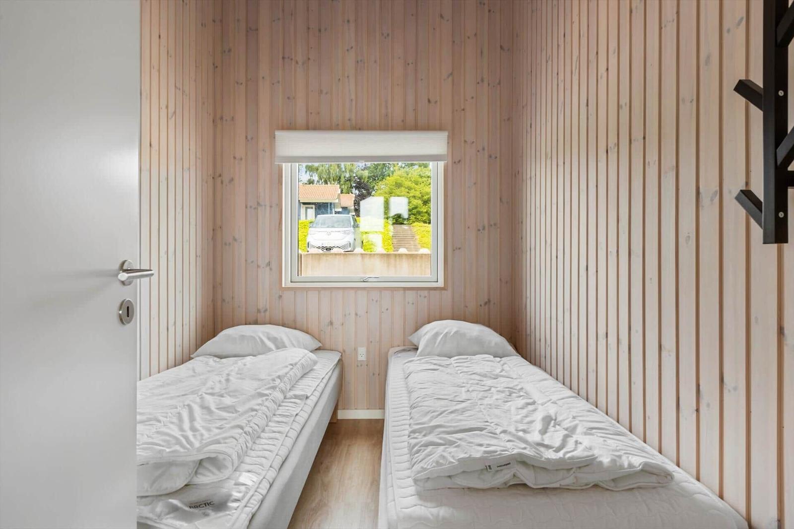 Two beds in a room with wooden walls and window view of outside area.