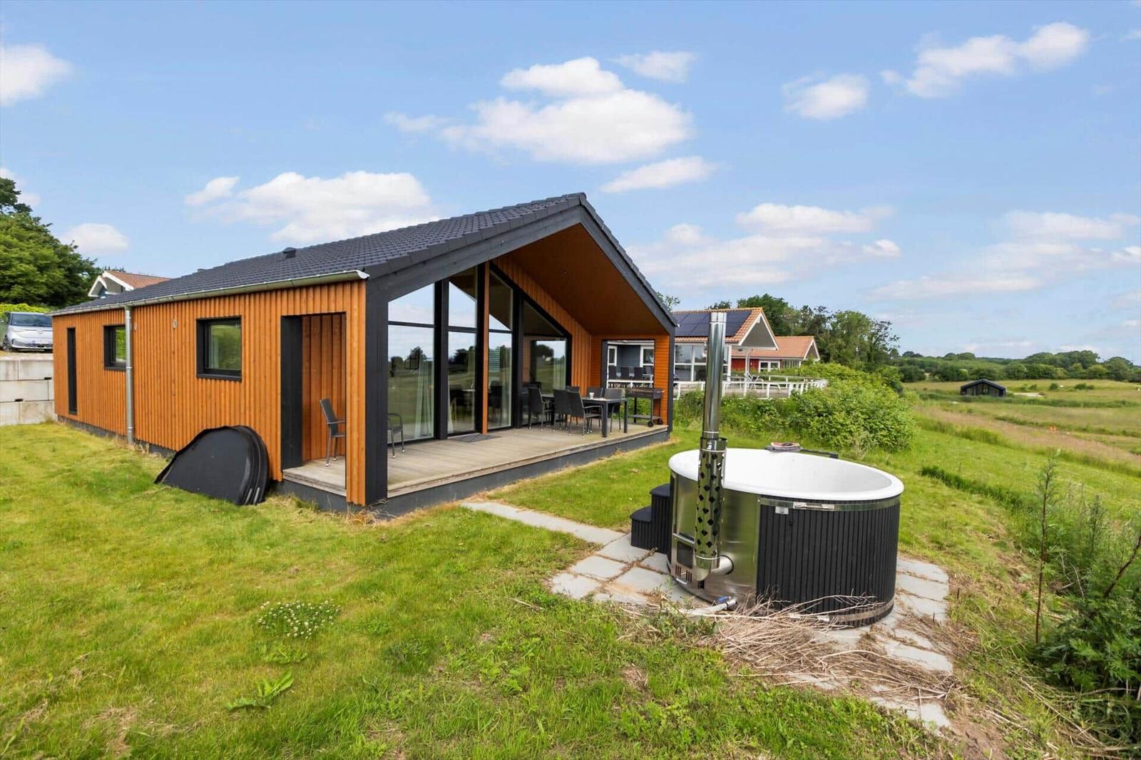 Modern wooden cabin with terrace and hot tub in grassland