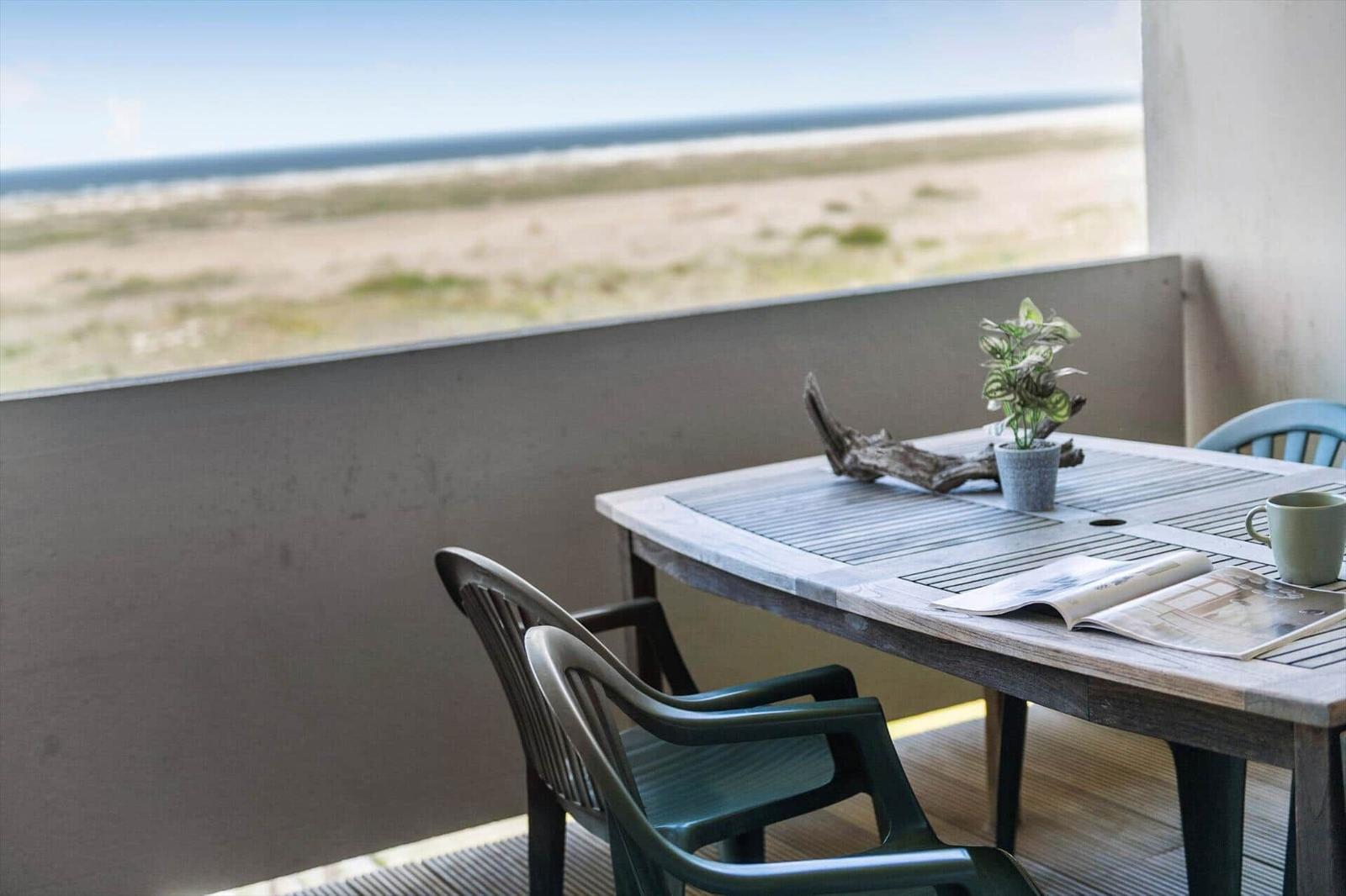 Terrasse mit Tisch und Stühlen, Blick auf Strand und Meer.