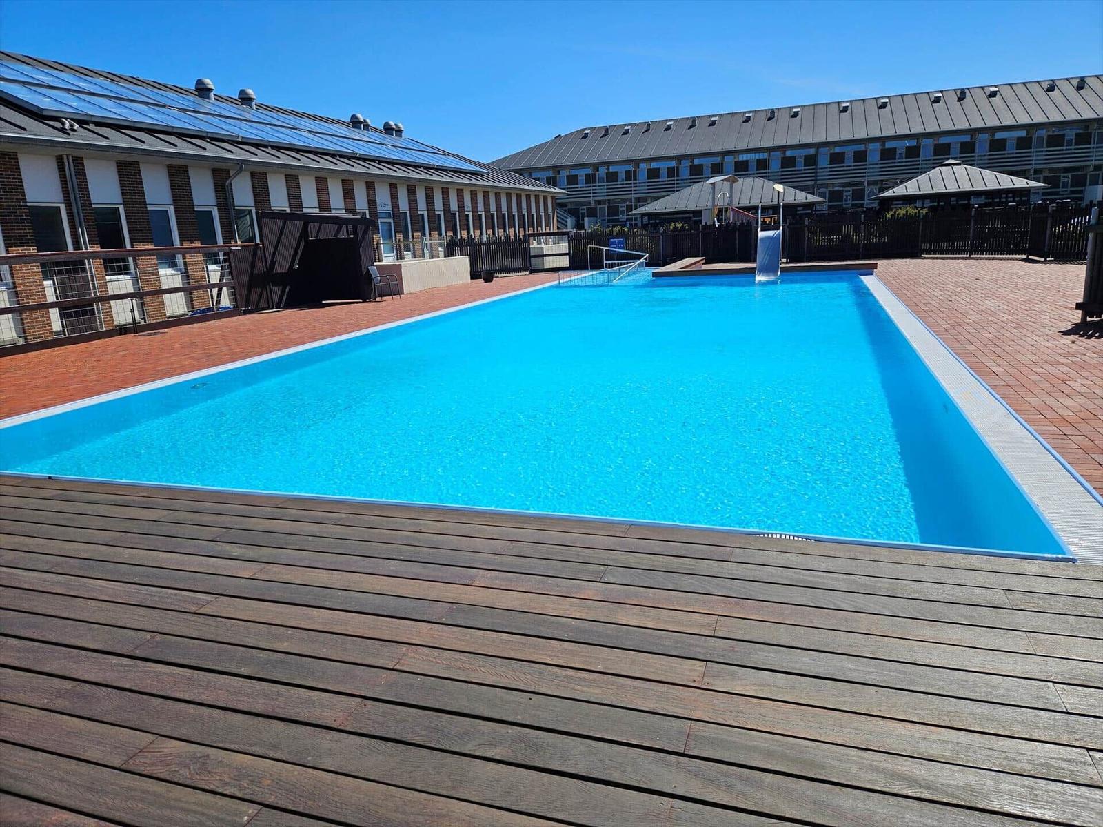 Ein klarer Swimmingpool mit Holzterrasse und modernen Gebäuden im Hintergrund.