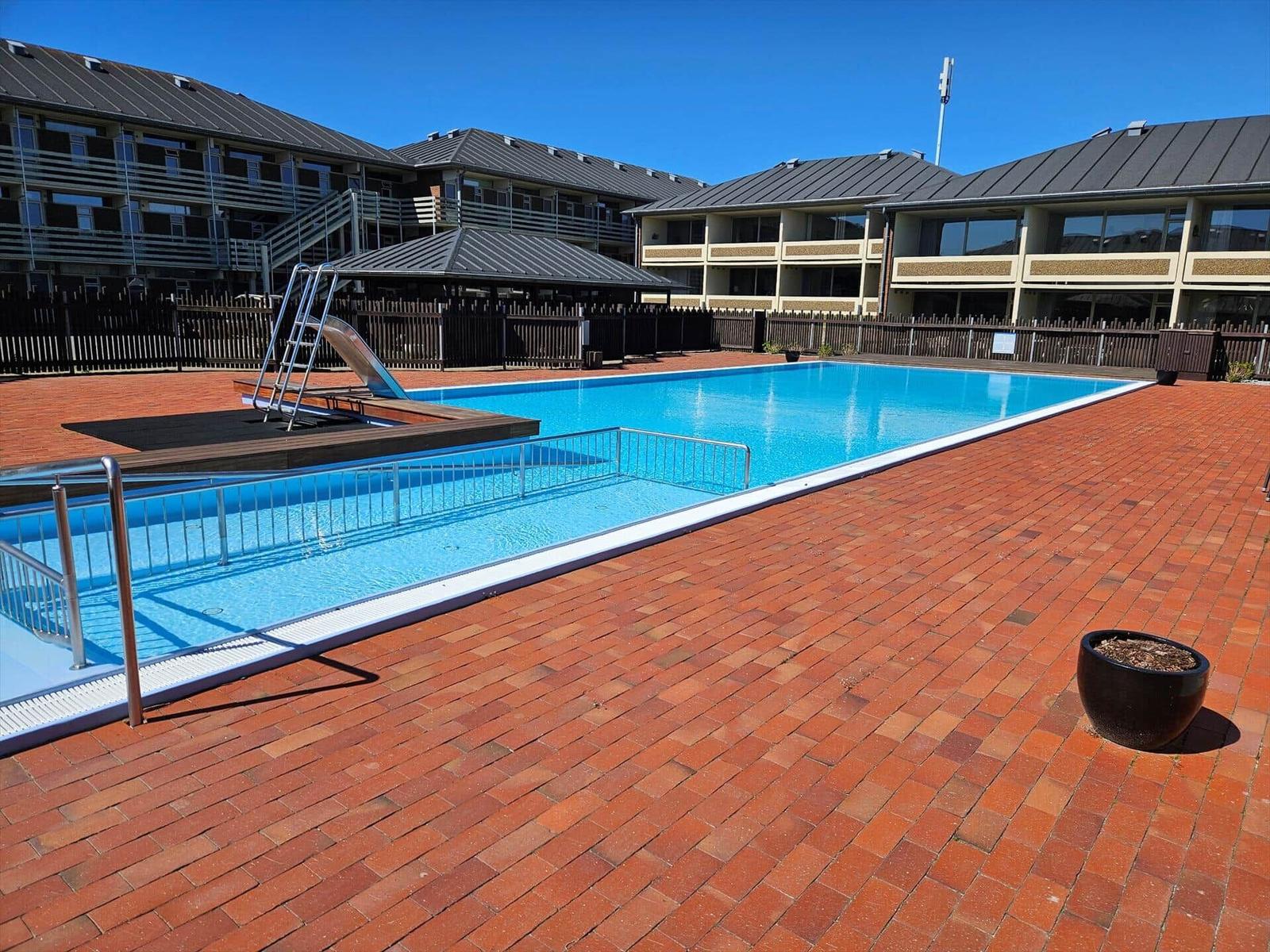 Pool mit Rutsche und Terrasse umgeben von mehrstöckigen Gebäuden.