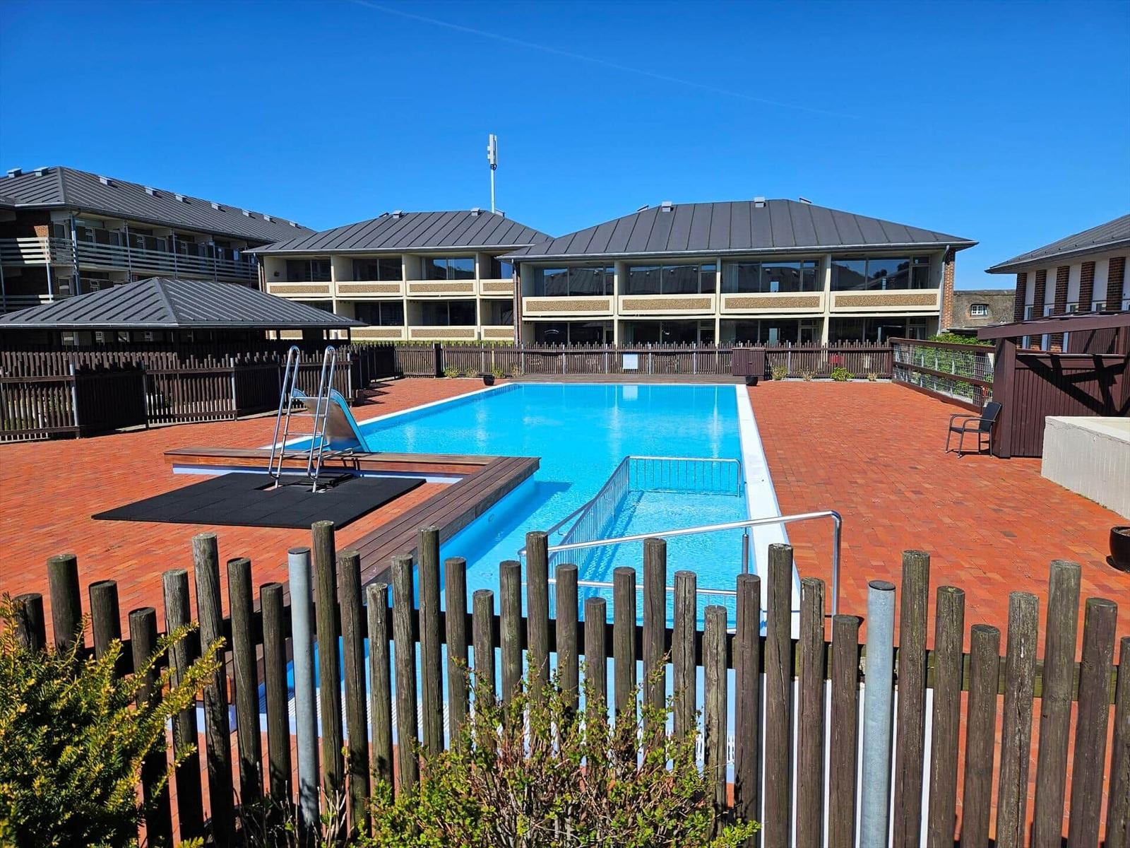 Pool mit Holzumrandung und mehrstöckigem Gebäude im Hintergrund.