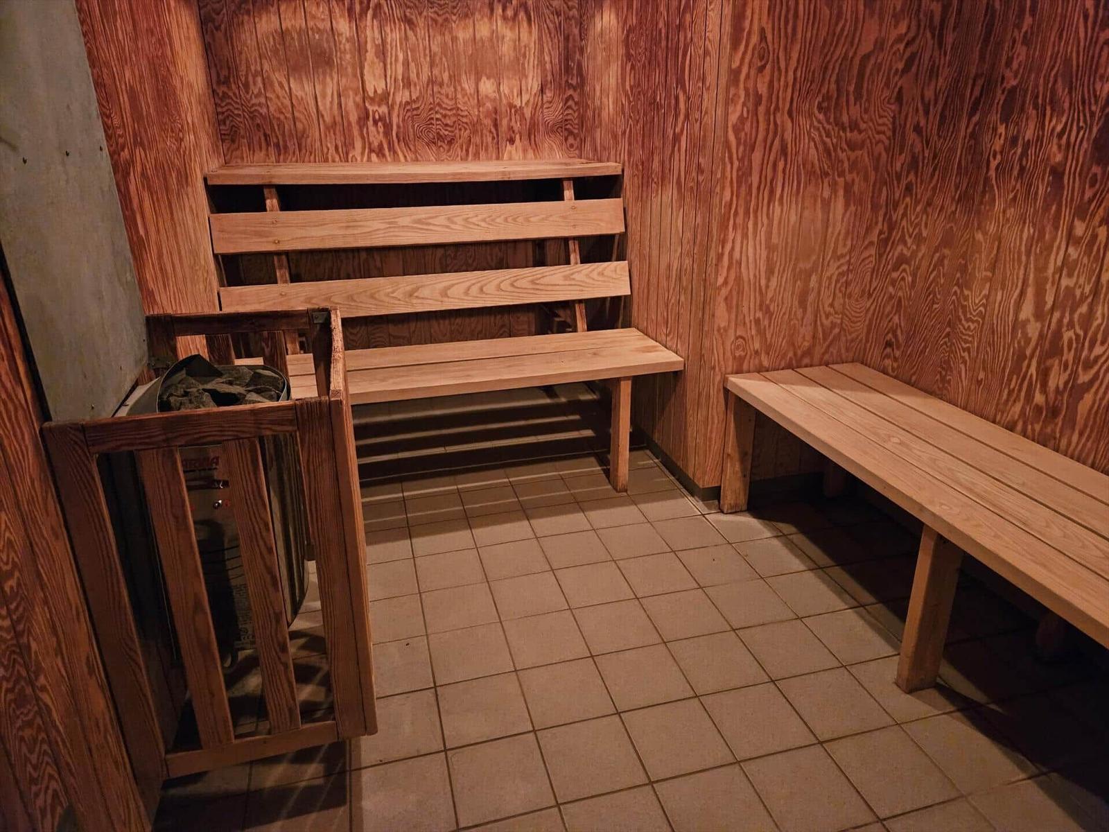 Sauna mit Holzwand, Bänken und Fliesenboden. Heizung im Hintergrund.