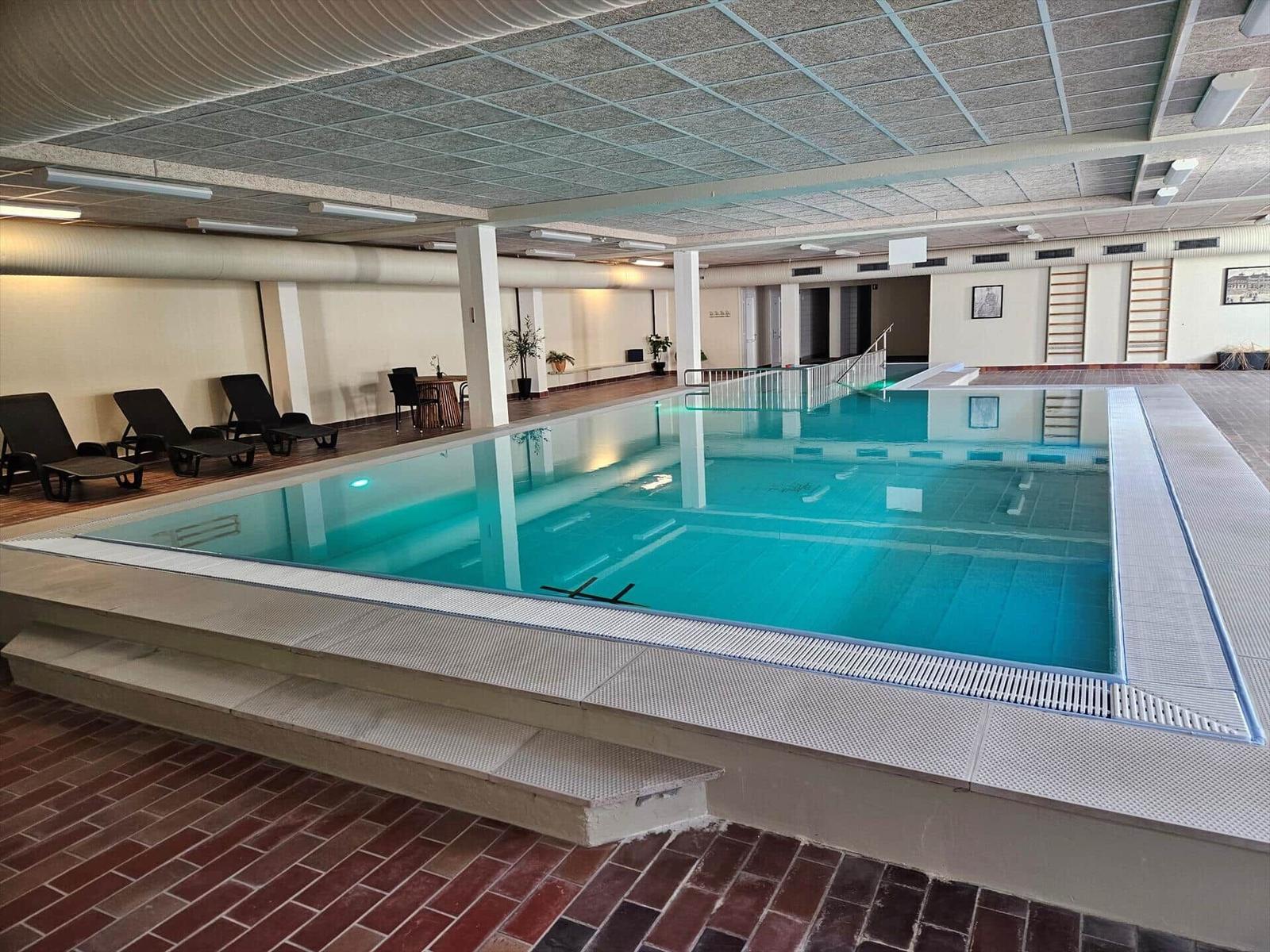 Innenpool mit Liegestühlen und Treppen zur Schwimmfläche.