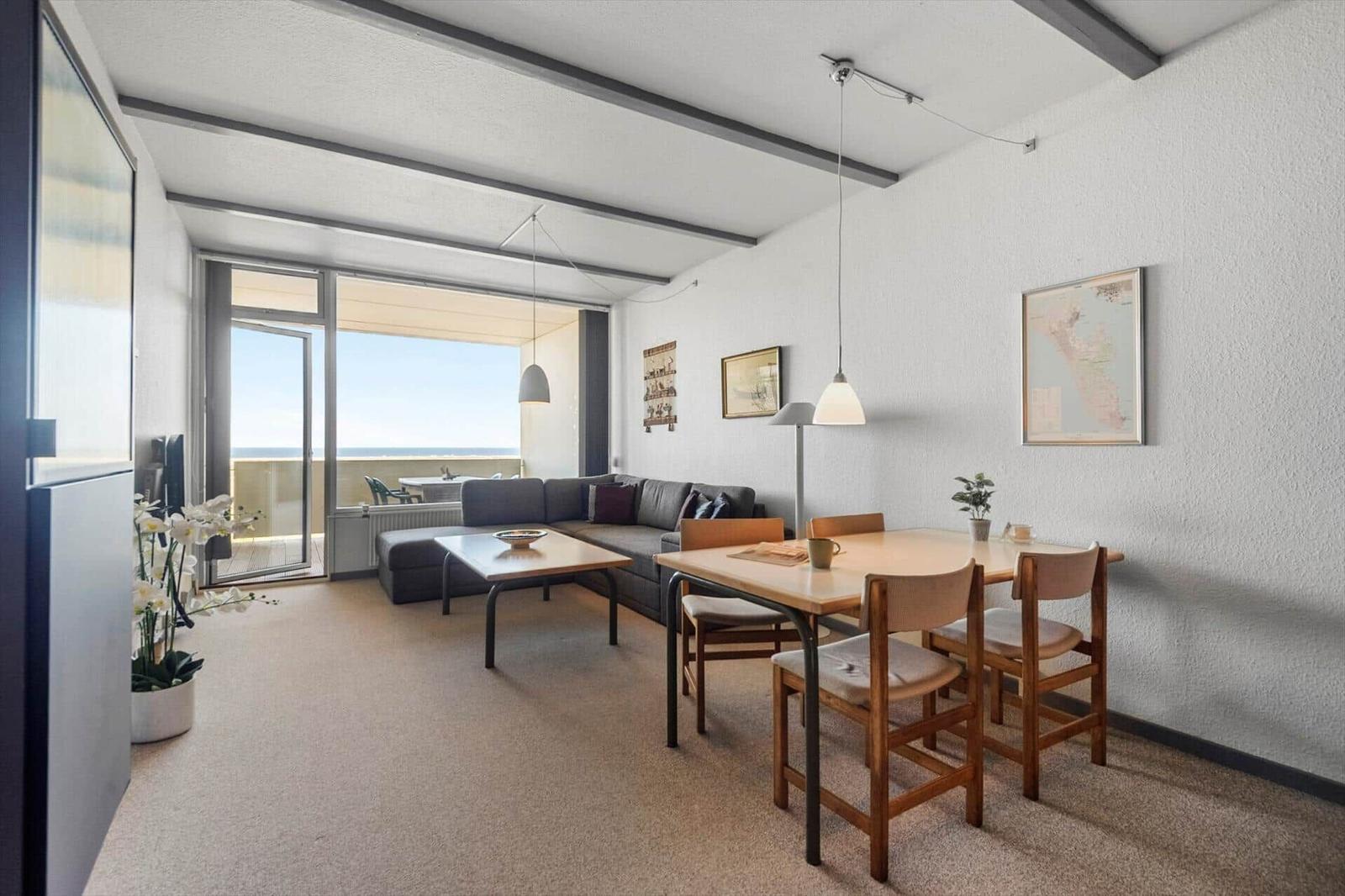 Wohn- und Essbereich mit Balkon, Sofa, Tisch und Stühle. Wandkarte und Pflanzen.