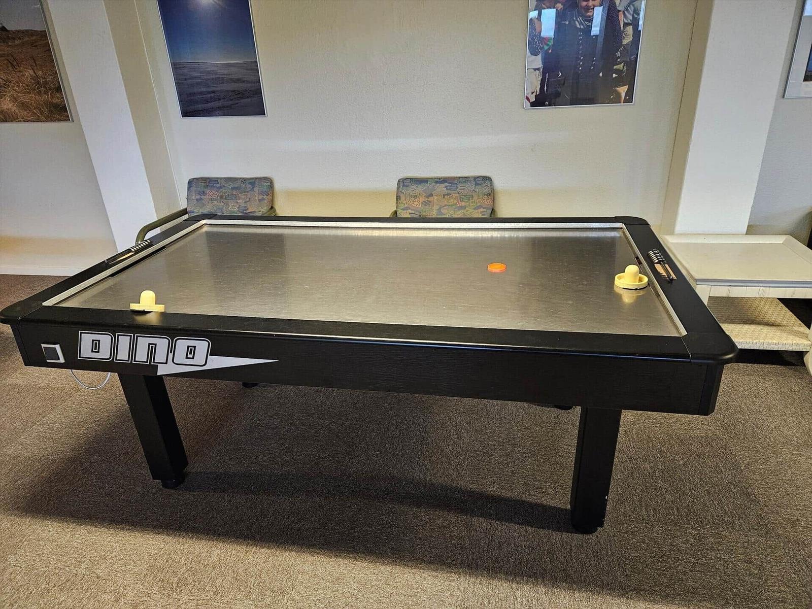 Ein Air-Hockey-Tisch mit zwei gelben Stöcken und einem orangefarbenen Diskett.