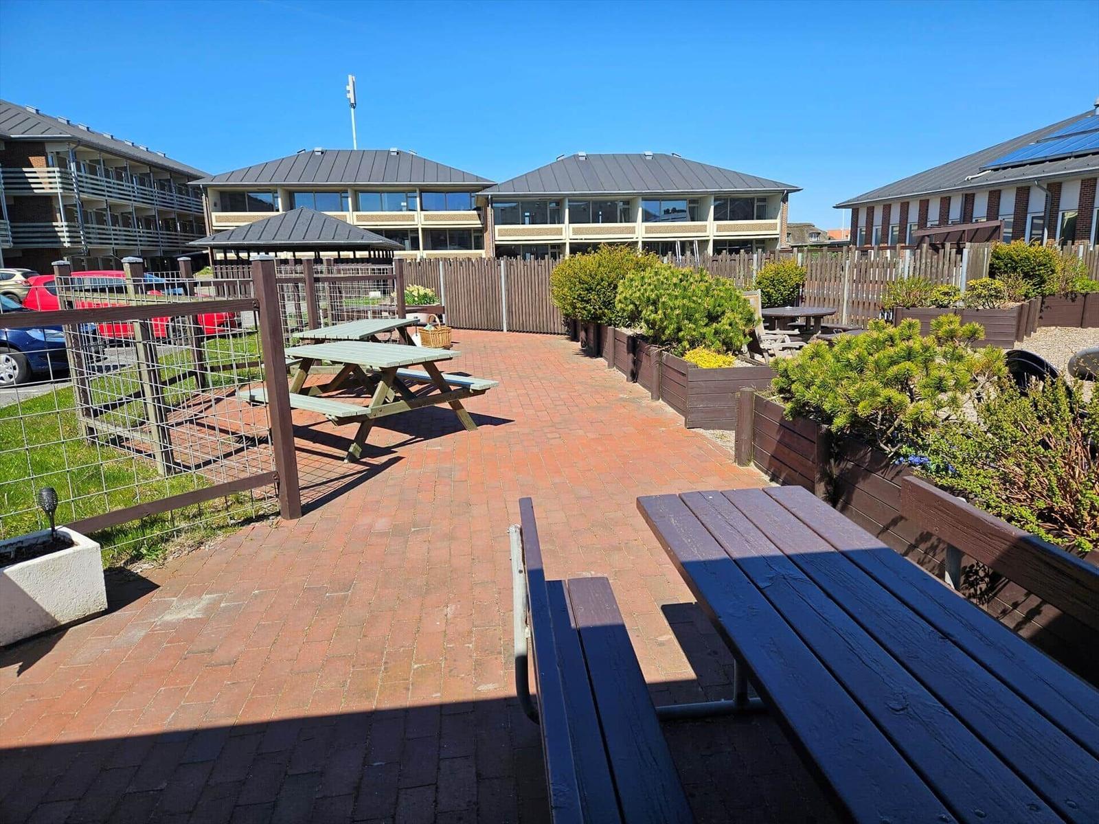 Terrasse mit Picknicktischen, Pflanzen und Wohnhäusern im Hintergrund.
