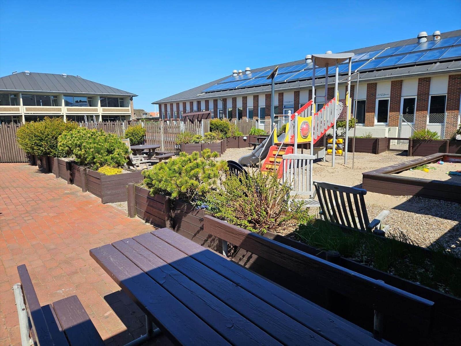 Terrasse mit Picknicktisch, Spielplatz und Gartenbereich vor Wohnhäusern mit Solaranlagen.