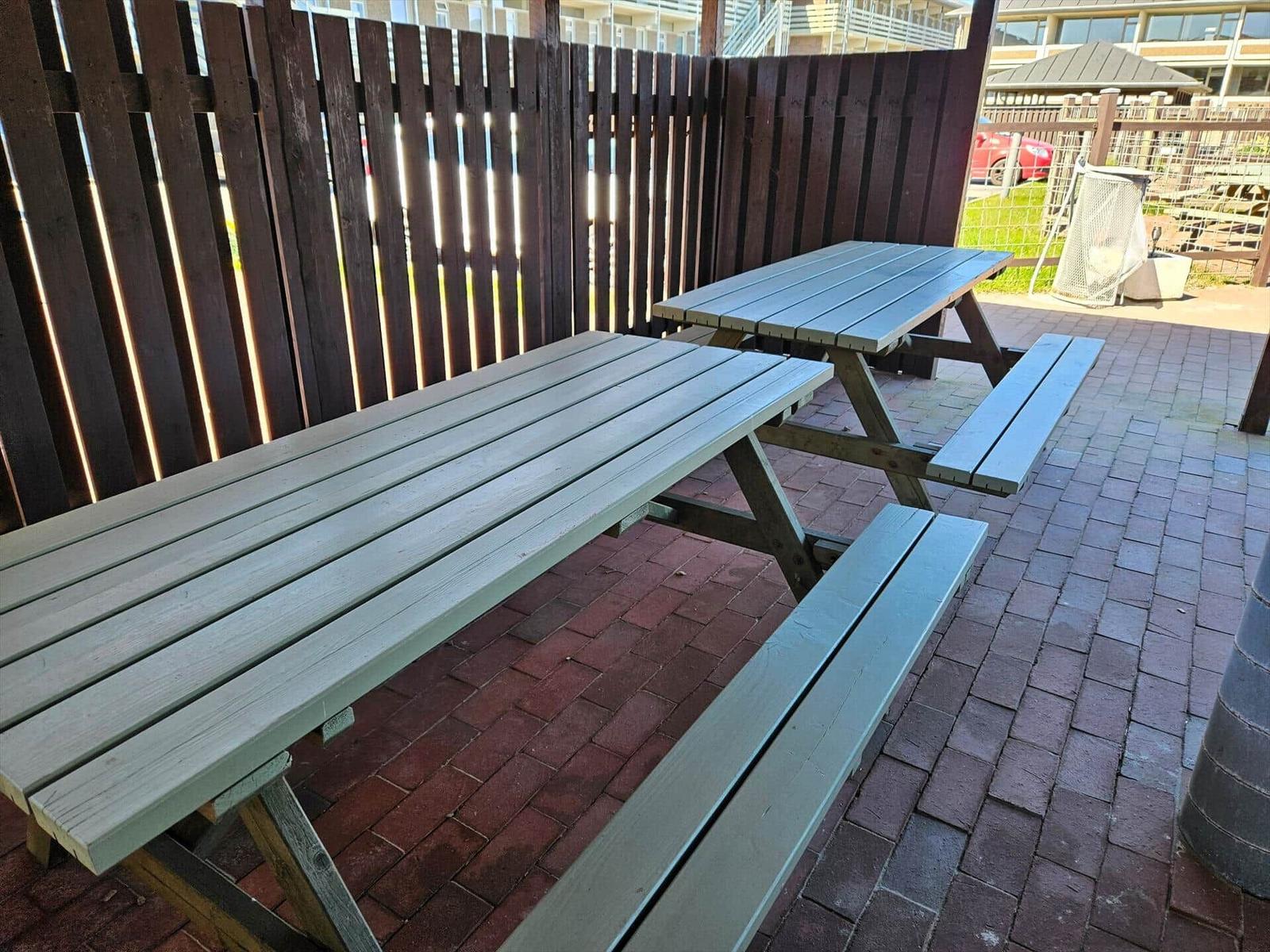 Zwei Holzpicknicktische auf gepflastertem Hof mit hölzerner Umzäunung.