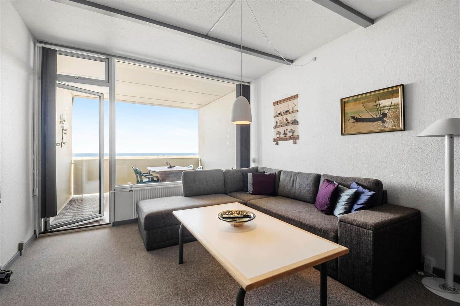 Wohnzimmer mit Sofa, Tisch und Balkonblick aufs Meer