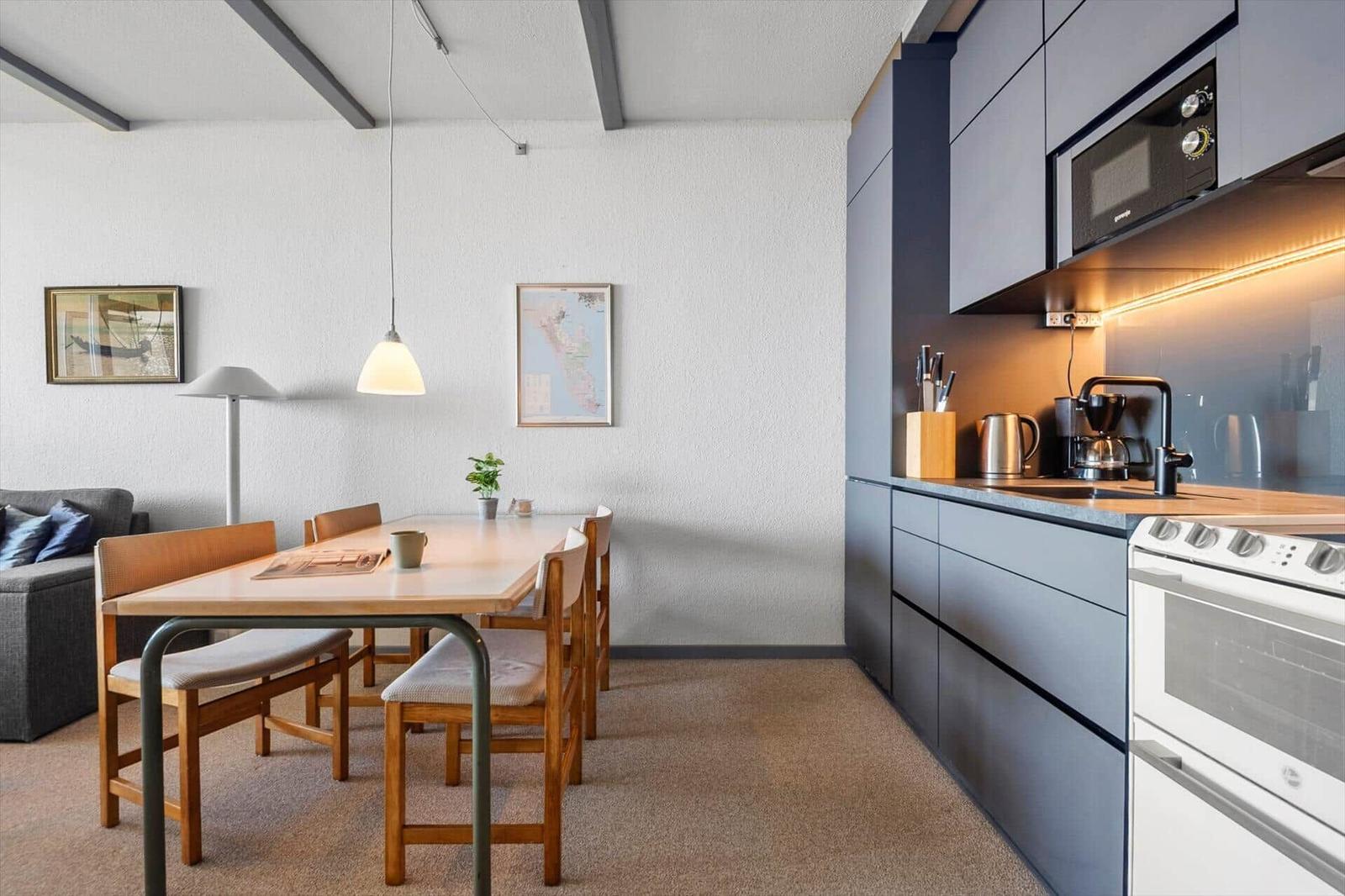Essbereich mit Tisch, Stühlen und Küchenzeile. Hintergrund: Wohnbereich mit Sofa.