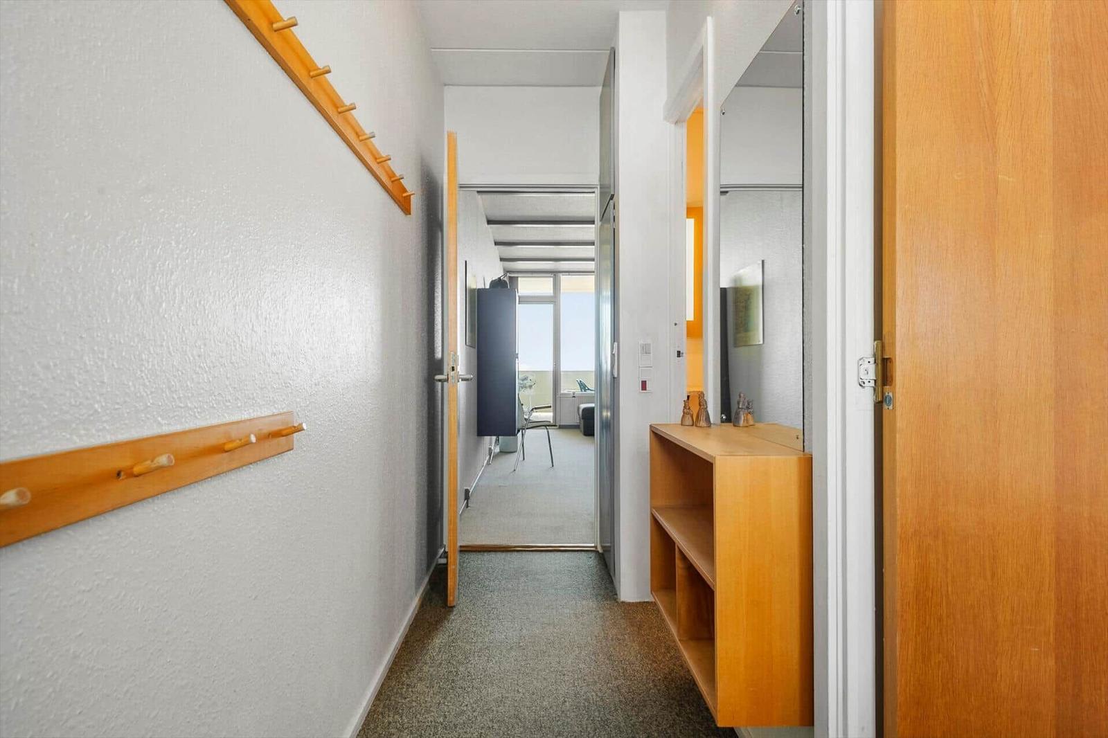 Flur mit Kleiderhaken, Spiegelschrank und Blick in Wohnbereich.