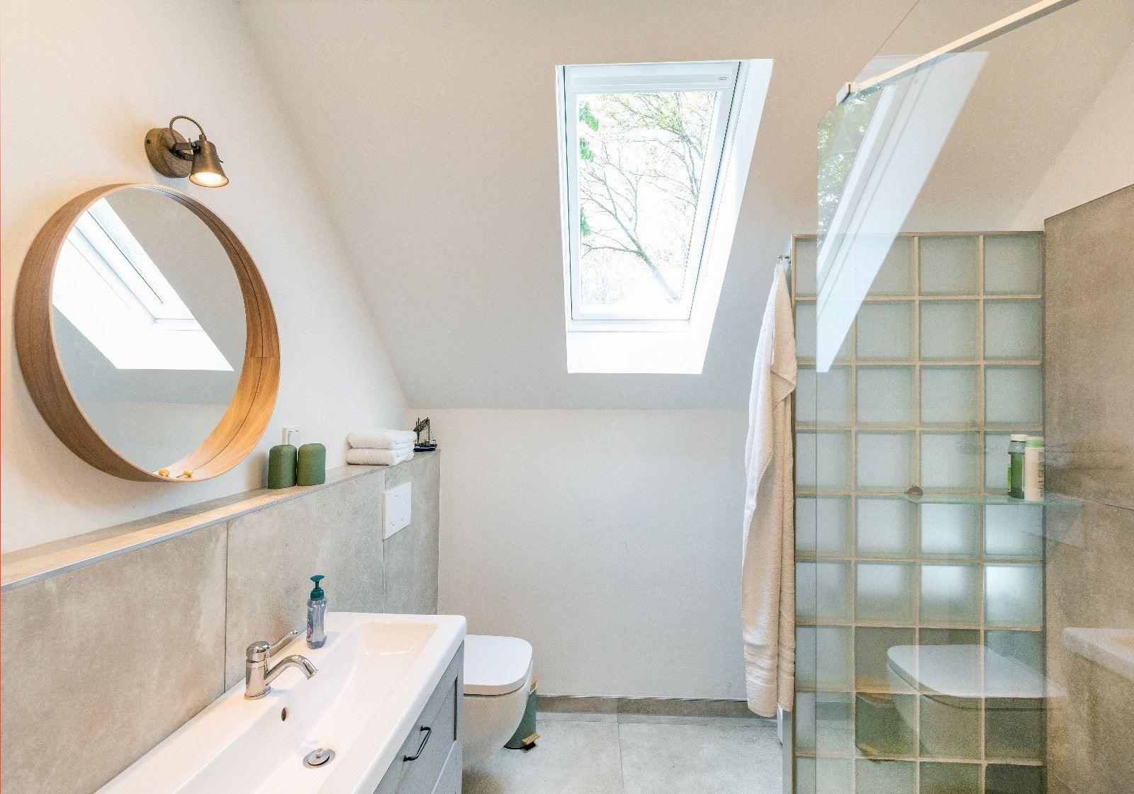 Badezimmer mit Dusche, Waschbecken und Dachfenster. Holzrahmen Spiegel und Glasfliesen.